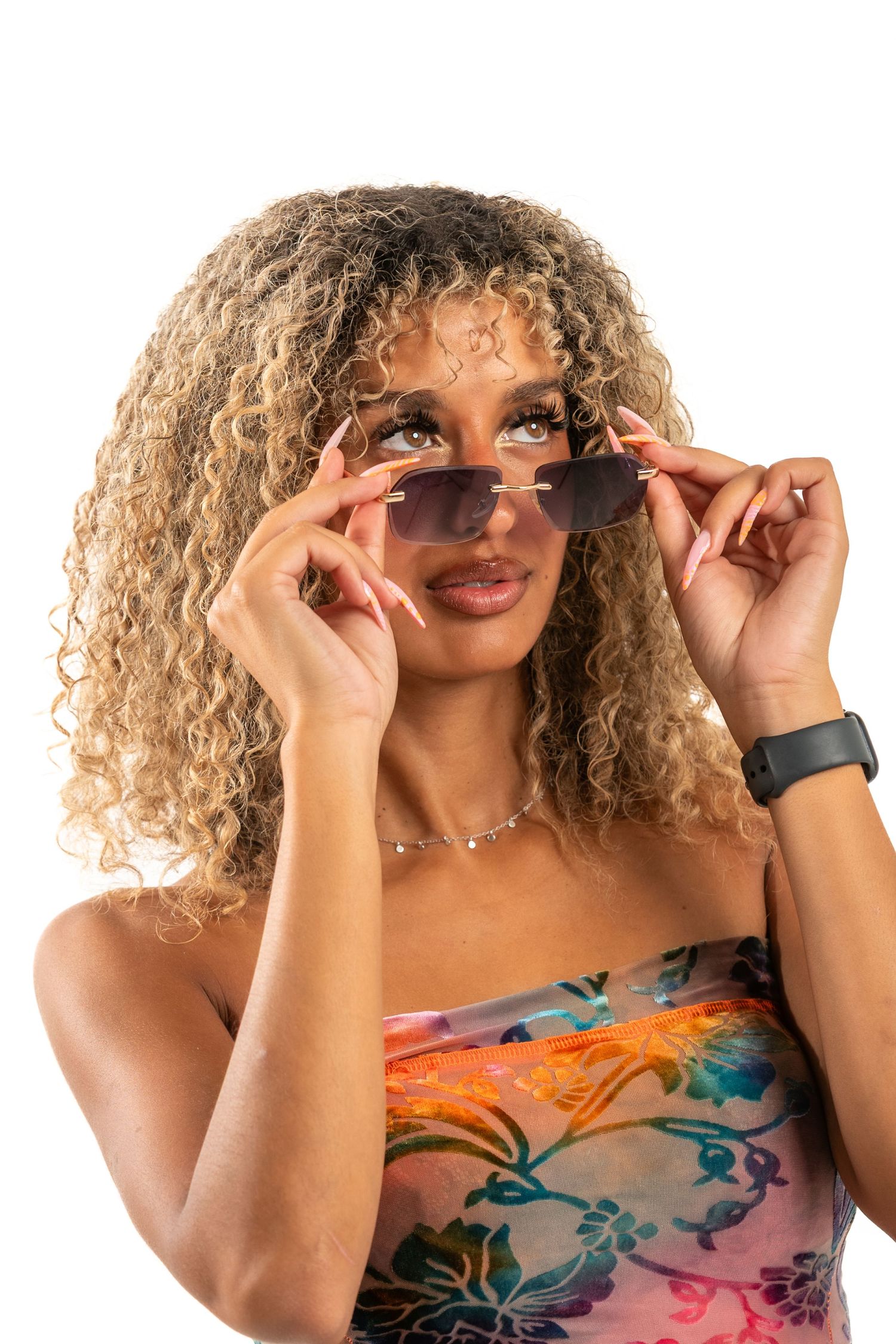 A person with curly blonde hair wearing sunglasses and a floral dress poses playfully in a photo series.