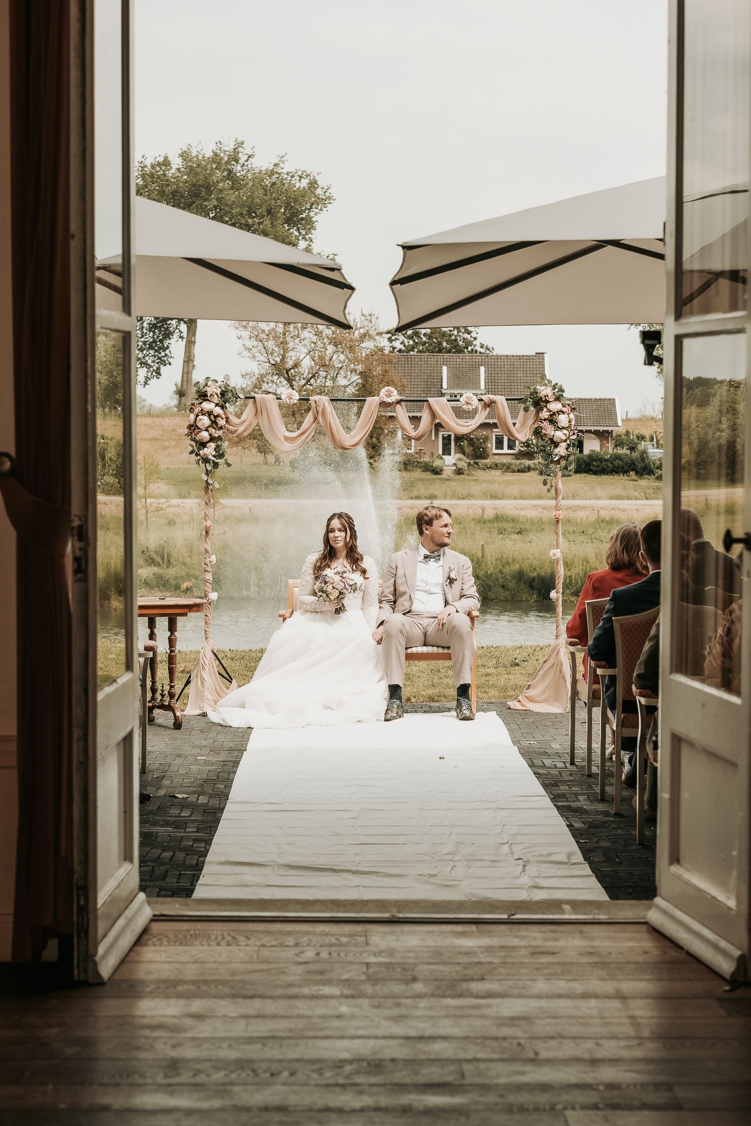 Wedding party in white dresses relaxing on outdoor deck with umbrellas and rustic decor at countryside venue.