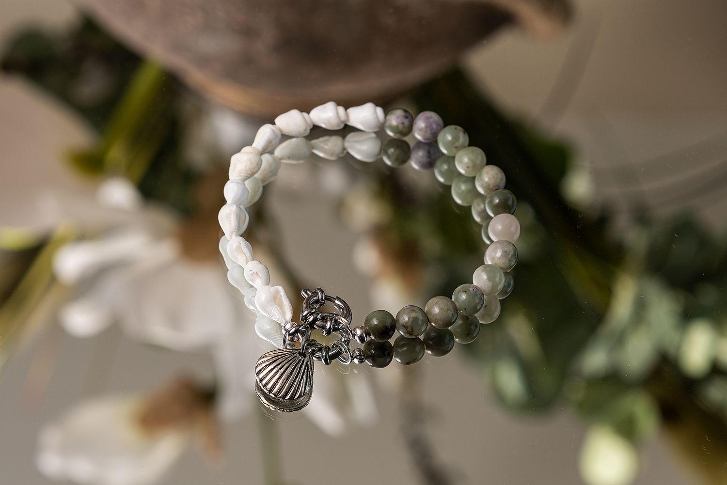 A delicate bracelet with white beads and silver charms displayed on a blurred natural background.