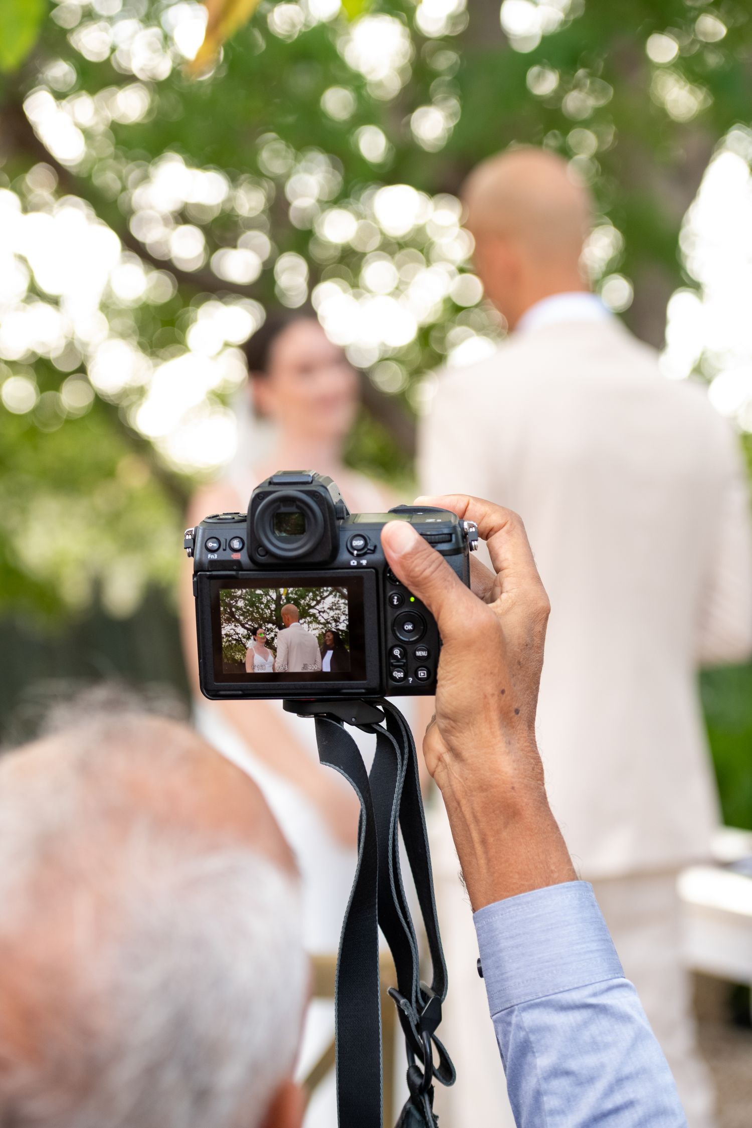 Photographer holds up a DSLR camera to capture an outdoor event with blurred bokeh background.