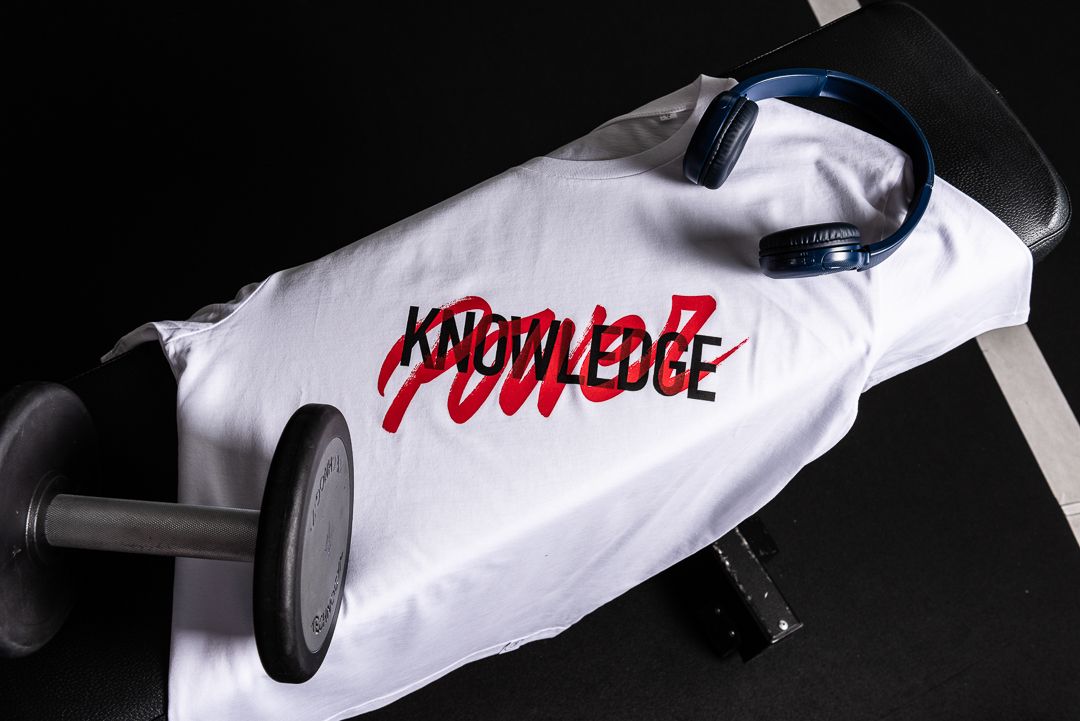 A white t-shirt with red 'Power' text graphic displayed on a clothing rack against dark background.