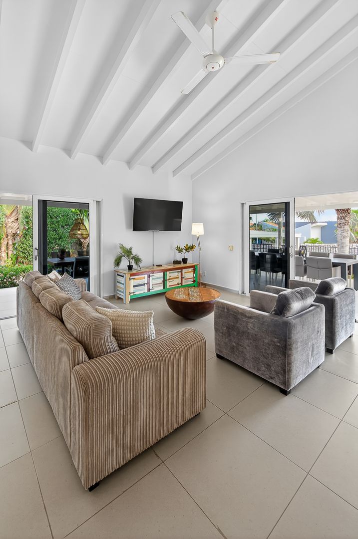 Bright open-plan living room with vaulted white beam ceiling, large corner sofa, TV unit, and sliding doors to outdoor patio.