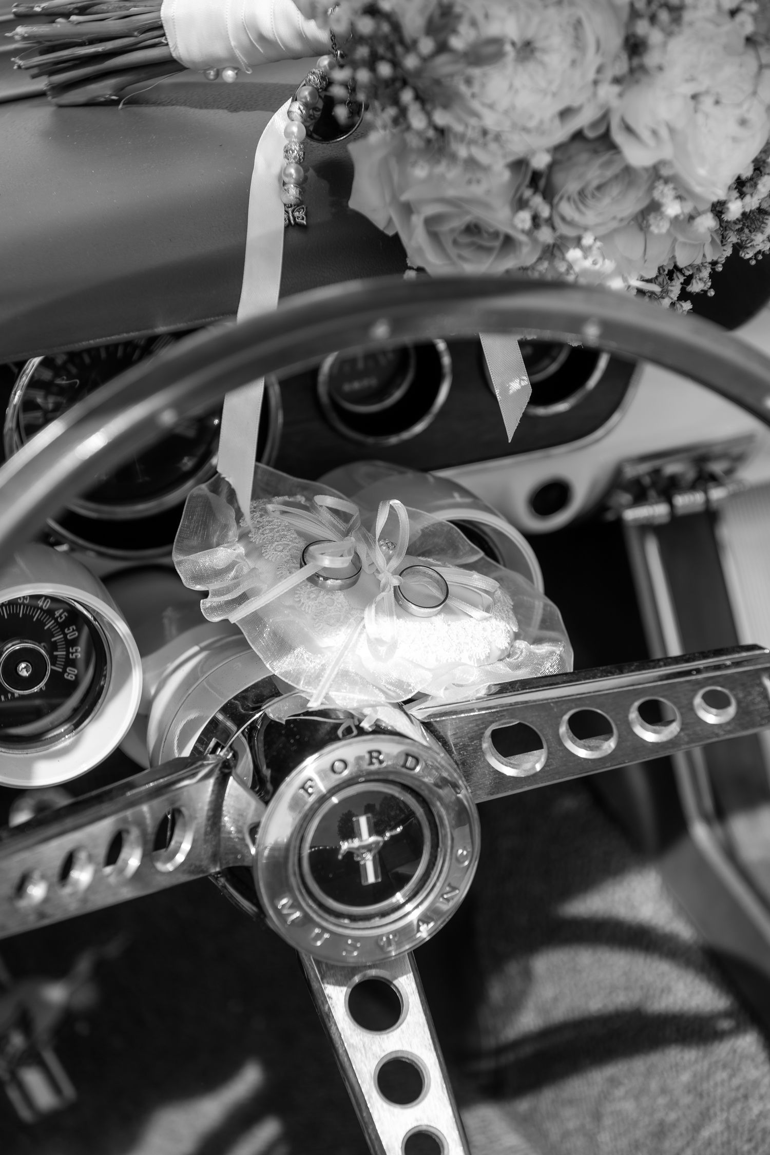 Black and white close-up photo of a classic Ford Mustang steering wheel and dashboard controls.