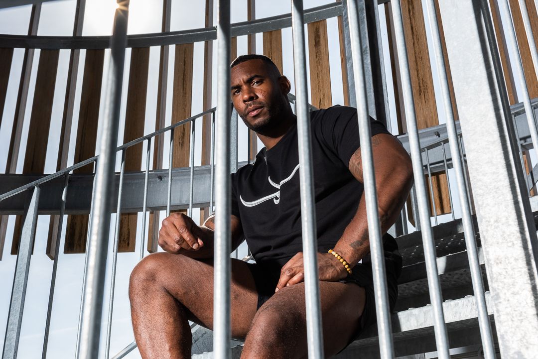 Muscular athlete in black tank top sitting on metal staircase during workout session.