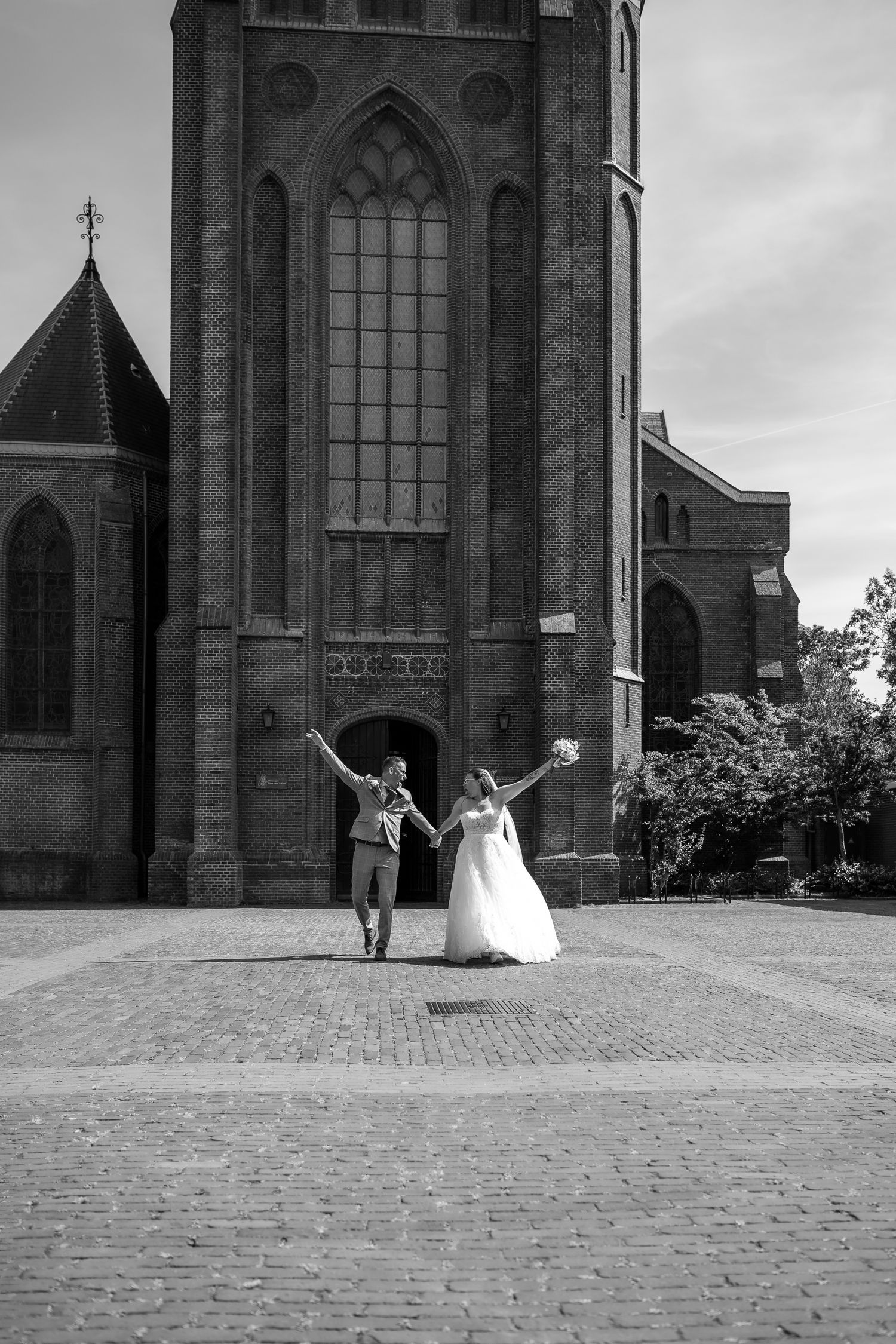 A black and white sequence of four wedding photos showing a couple celebrating outside a gothic church cathedral.