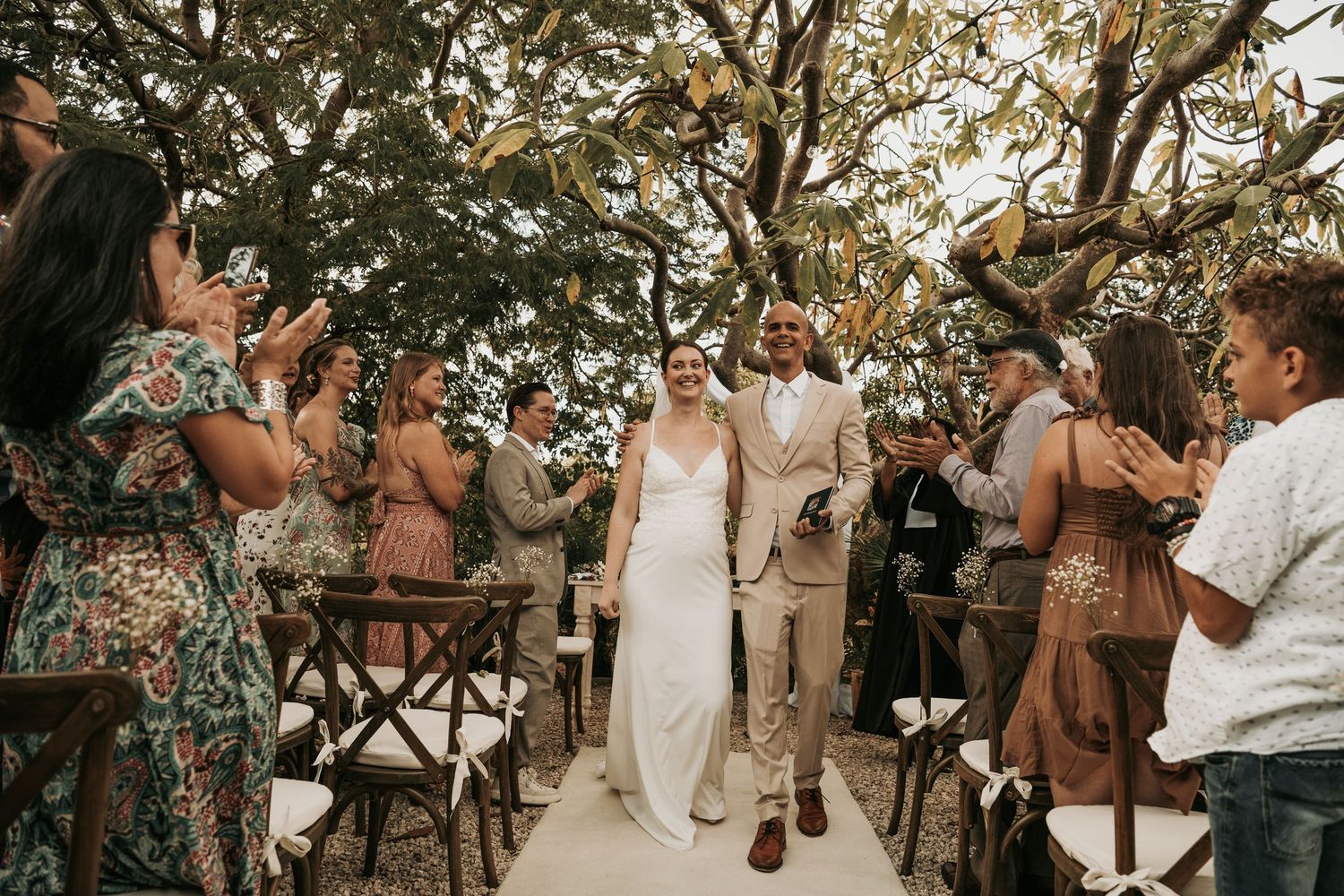 Wedding guests dance and celebrate during a sunset reception under rustic string lights in an outdoor garden setting.