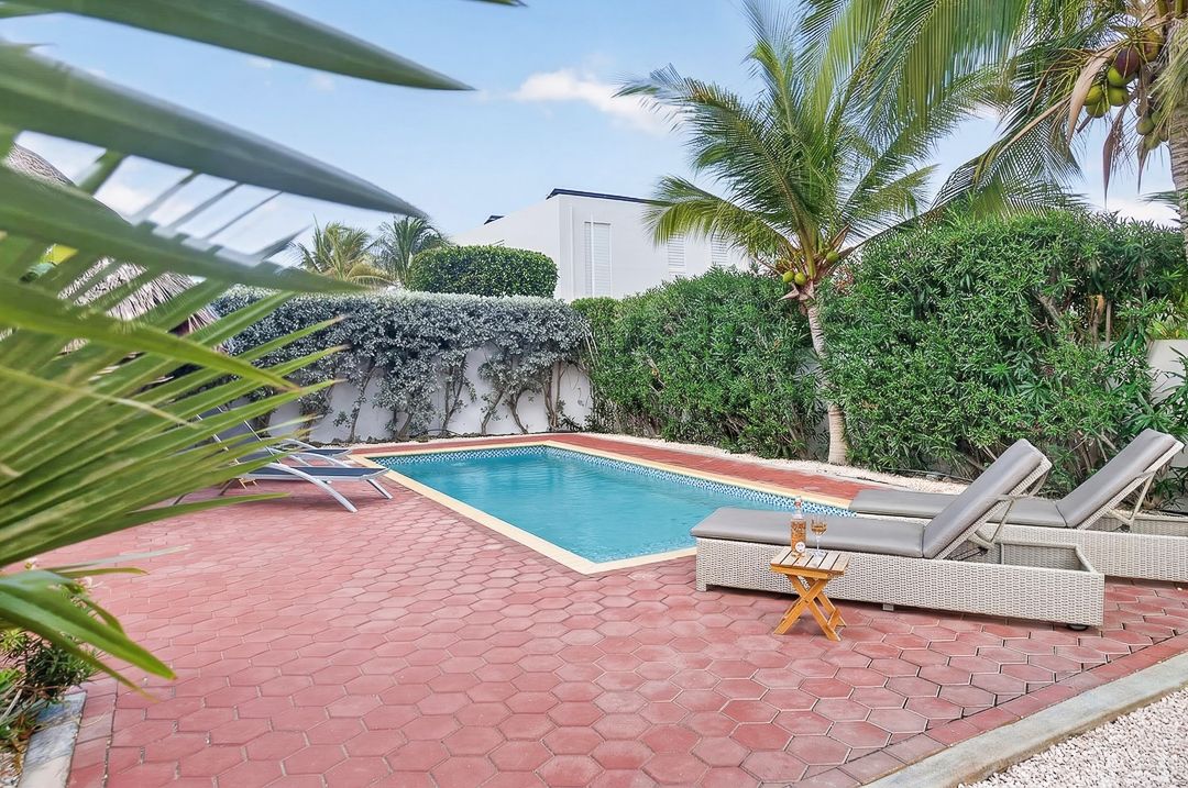 Private backyard pool surrounded by brick pavers, lounge chairs, and lush tropical palms in a serene outdoor setting.