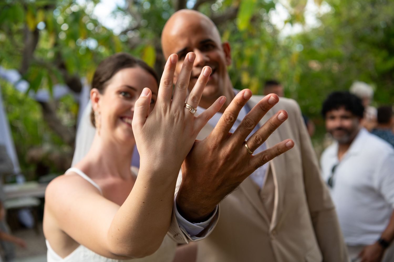 People raise their hands in a celebratory gesture while standing outdoors in a green park setting.