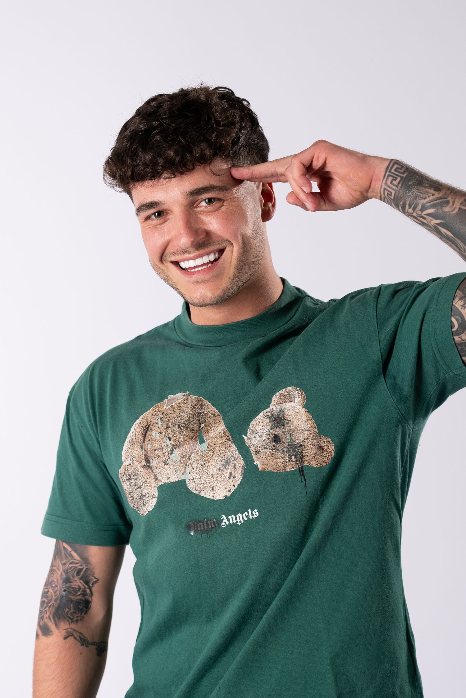 Person wearing a green t-shirt with a light-colored koala graphic design smiles and poses against white background.