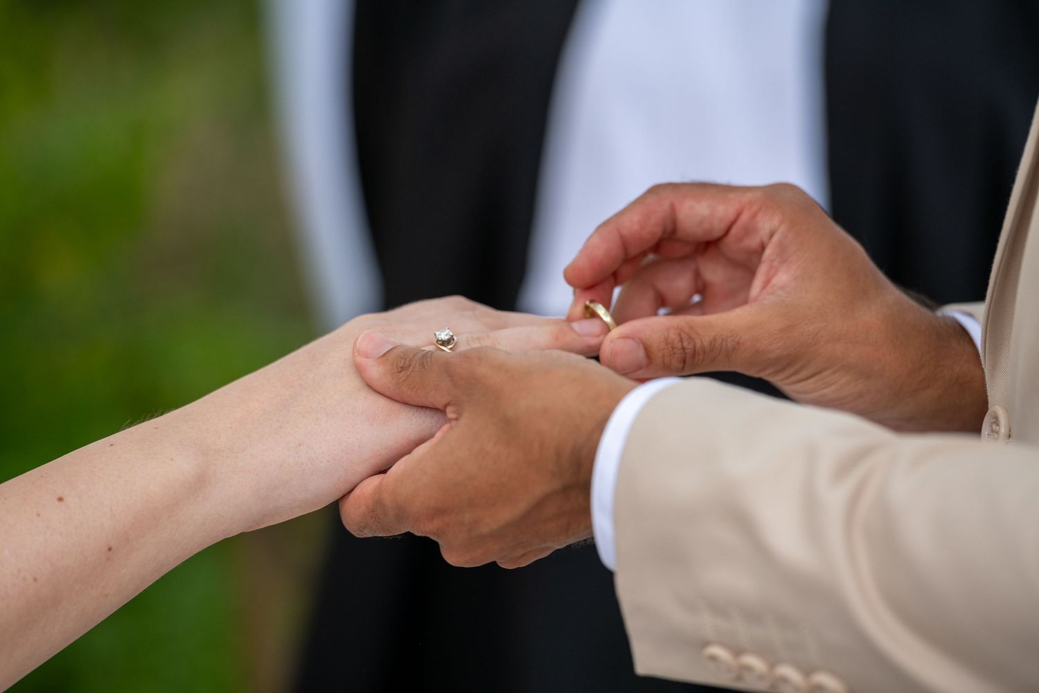 Close up of hands exchanging wedding rings during an outdoor ceremony.