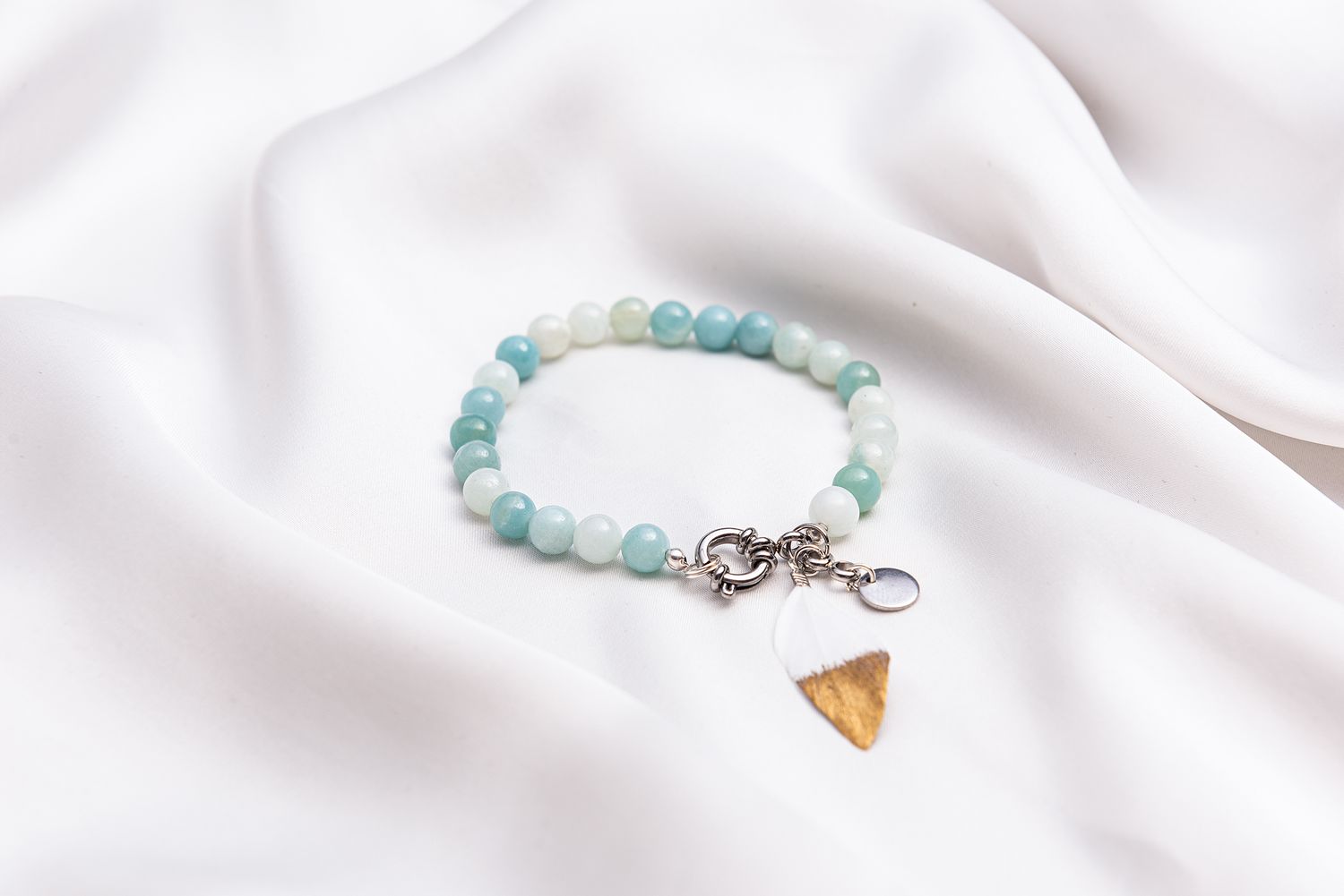 Elegant beaded bracelet with aqua blue and white stones connected by a silver clasp on white fabric.