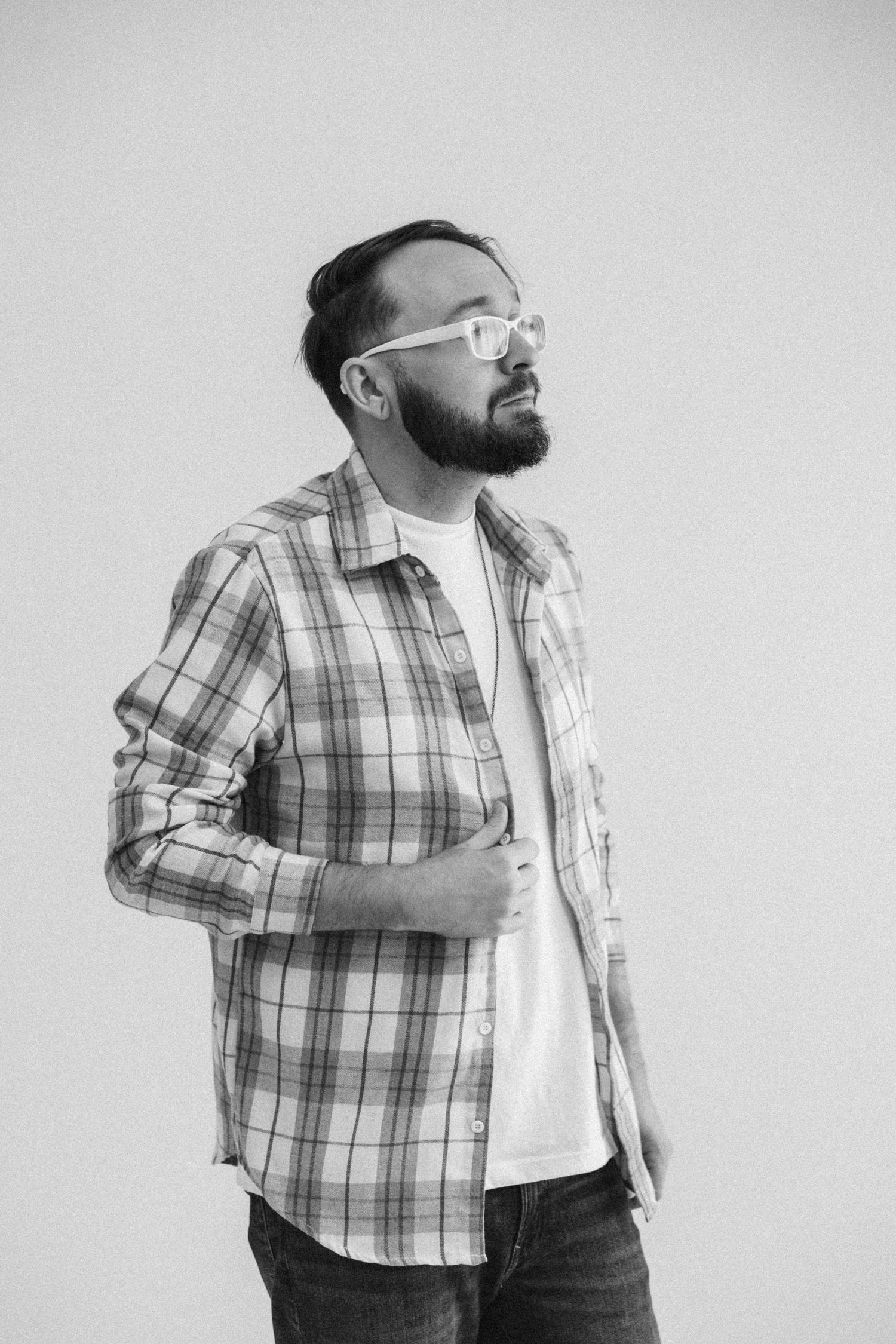 Man in plaid shirt posing expressively against white background in black and white series.