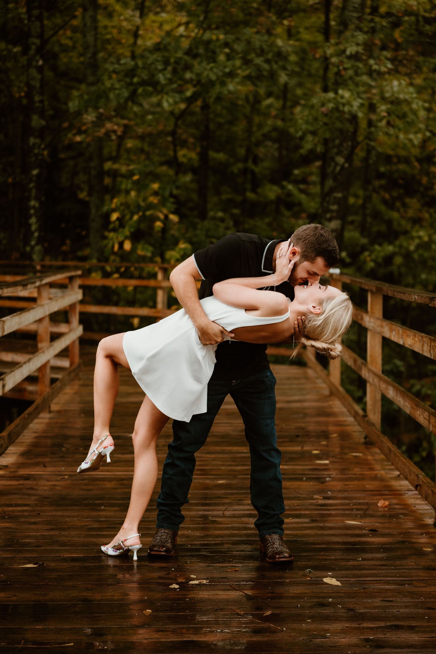A romantic dip pose on a wooden bridge surrounded by lush greenery.