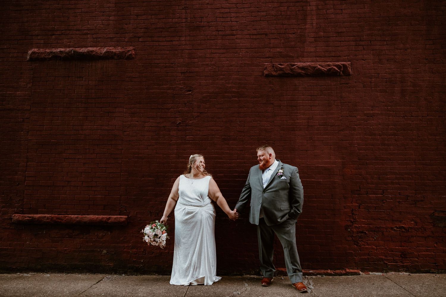 Wedding couple posed against rustic red brick wall background.