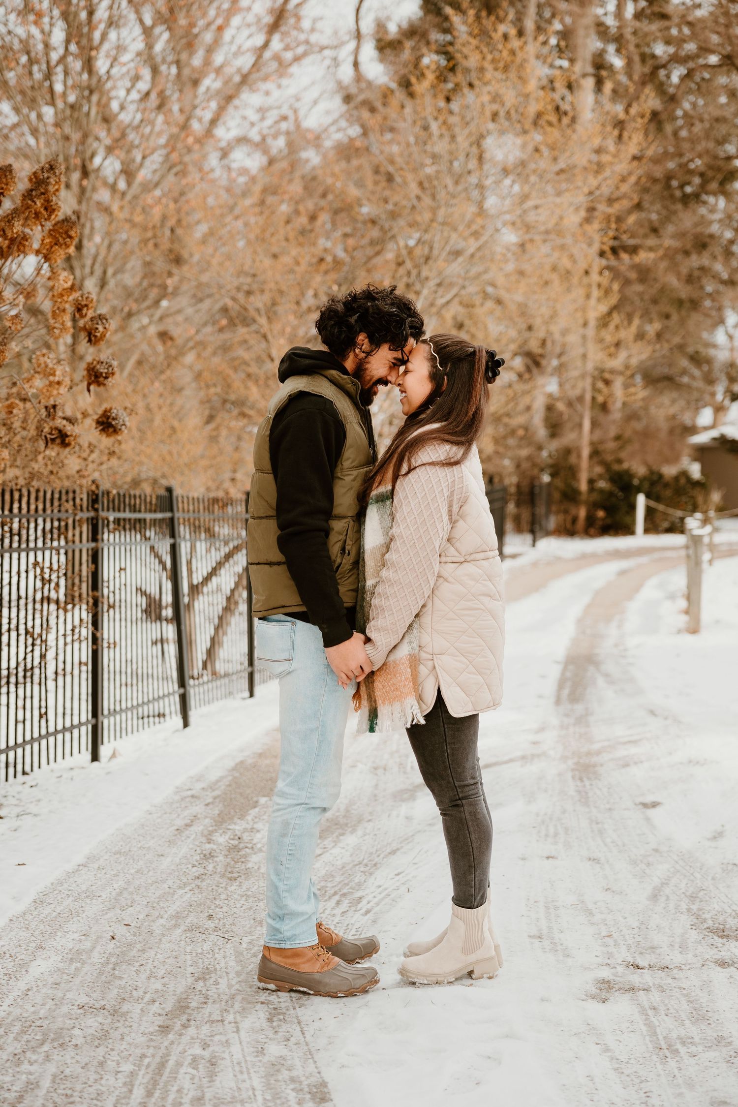 A couple shares a romantic moment on a snow-covered path surrounded by winter scenery.