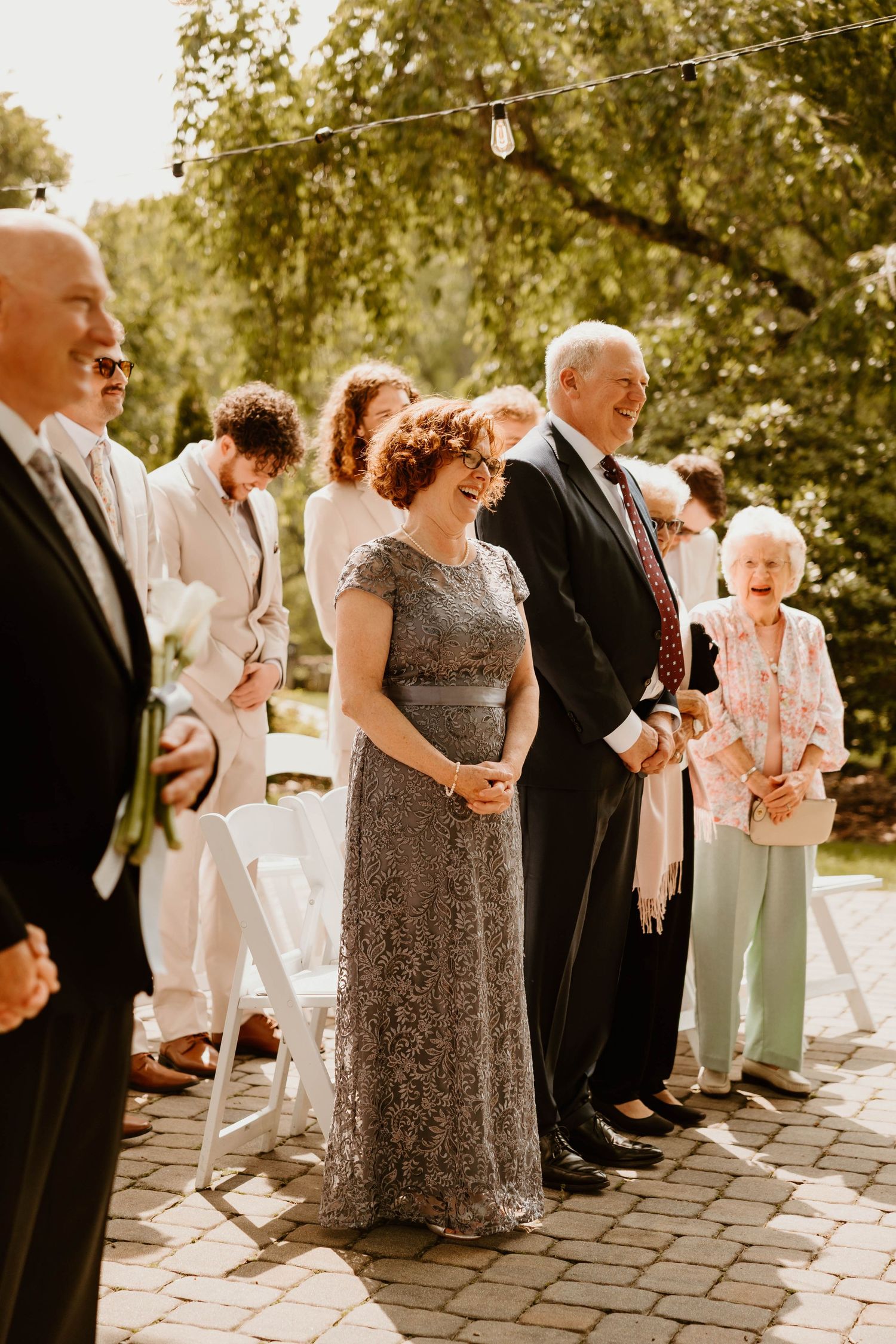 Wedding guests in formal attire gather outdoors on a stone patio during the celebration.