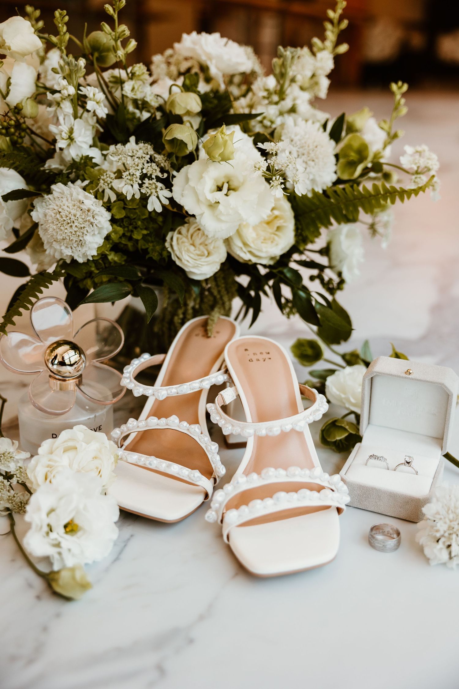 Delicate white bridal shoes and floral arrangements styled for wedding detail photography.