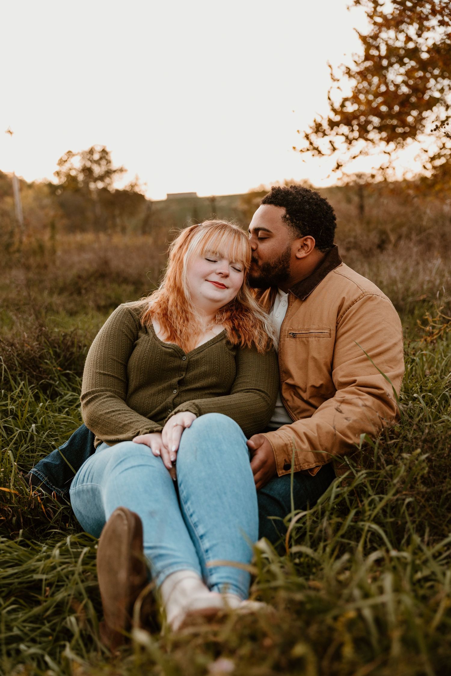 A romantic couple sits together in a grassy field during golden hour.
