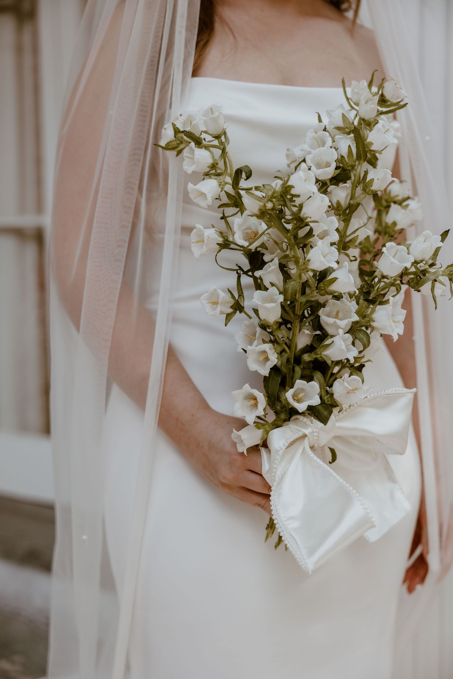 Close-up of white bell-shaped flowers in a bridal bouquet against a white dress.