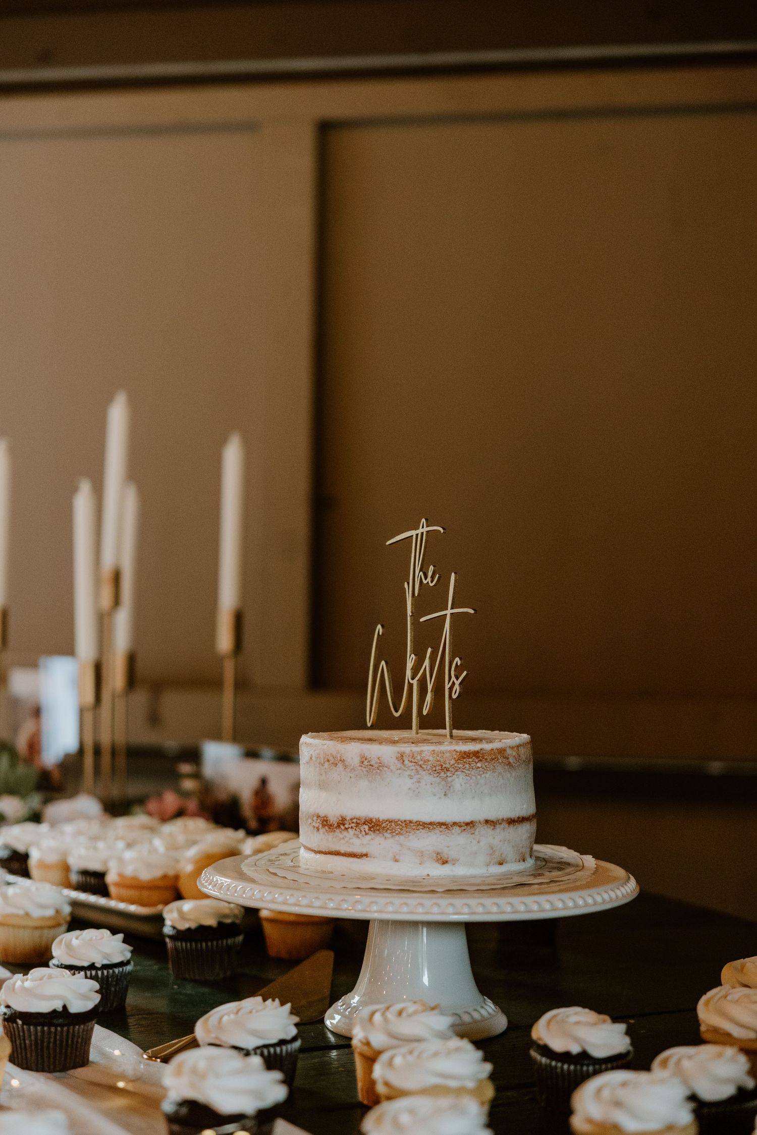 White wedding cake with delicate decorations displayed on cake stands alongside matching cupcakes.