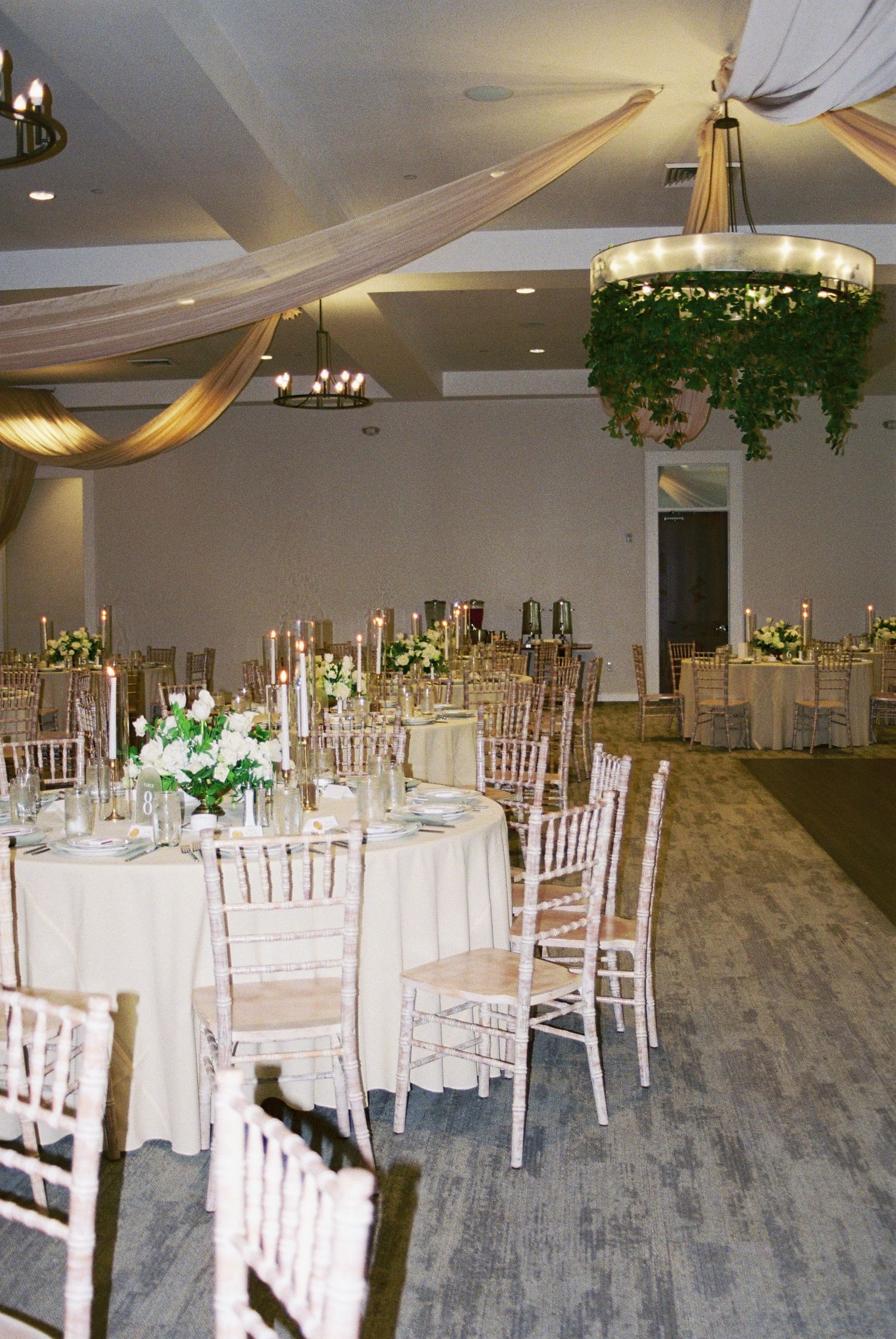 Elegant wedding reception hall with chiavari chairs, draped ceiling fabric, and floral chandelier centerpiece.