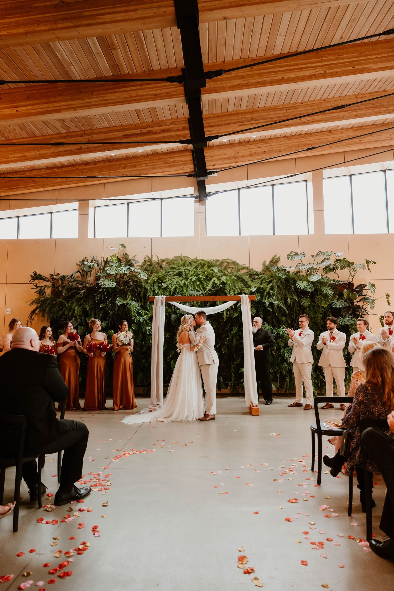 Indoor wedding ceremony with floral arch and scattered rose petals.