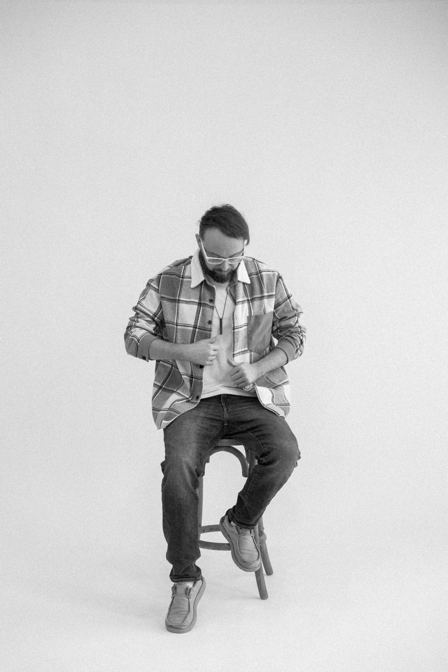Person in plaid shirt and jeans sitting on stool in minimalist black and white photoshoot.