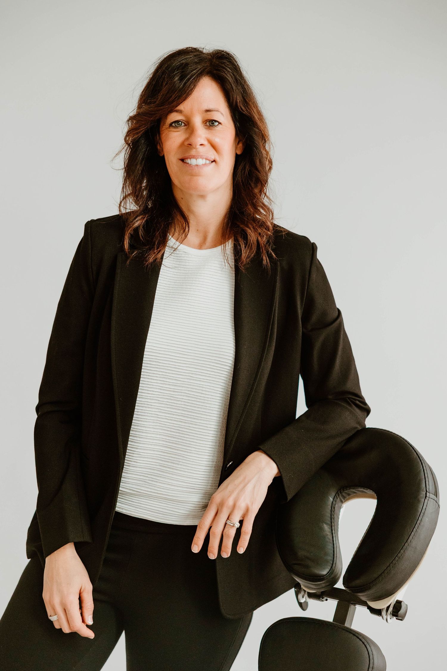 Professional business portraits in black blazer seated in office chair against white background.