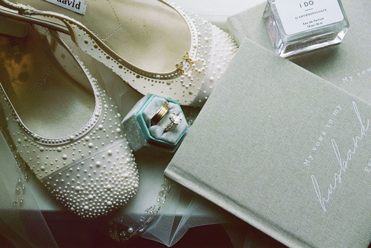 Pearl-embellished bridal flats, ring box with wedding bands, perfume, and a bridesmaid book flatlay.