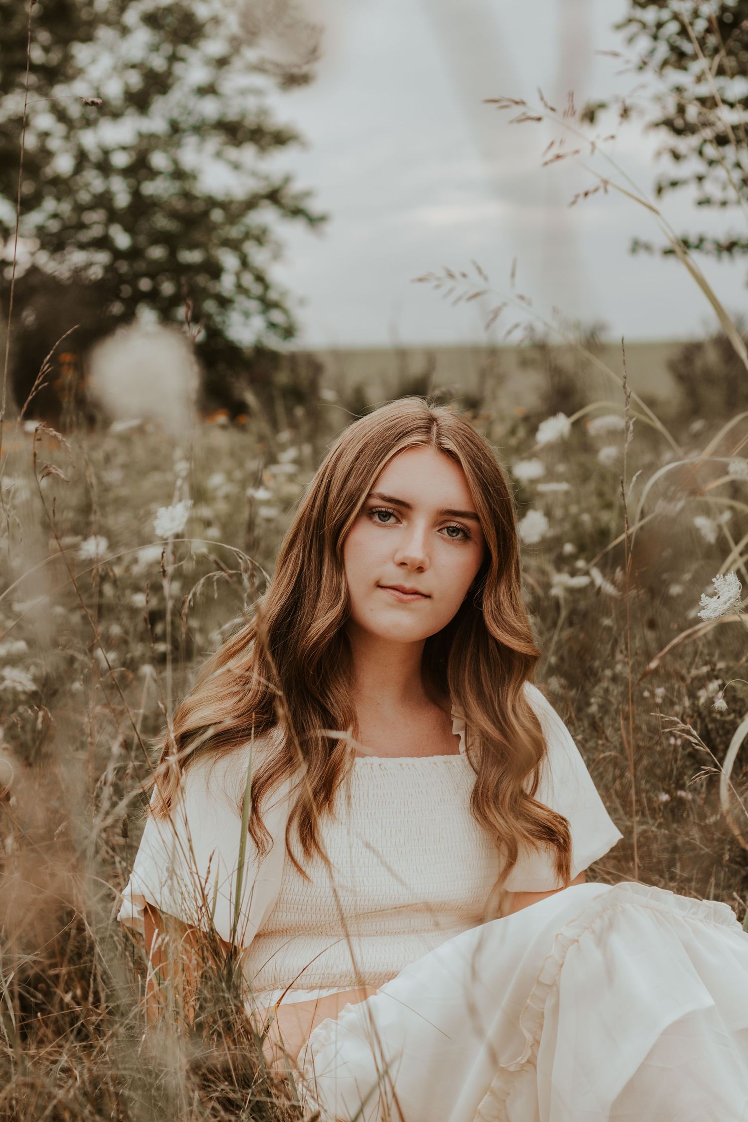 Ethereal outdoor portrait in a white dress among tall grass and wildflowers.