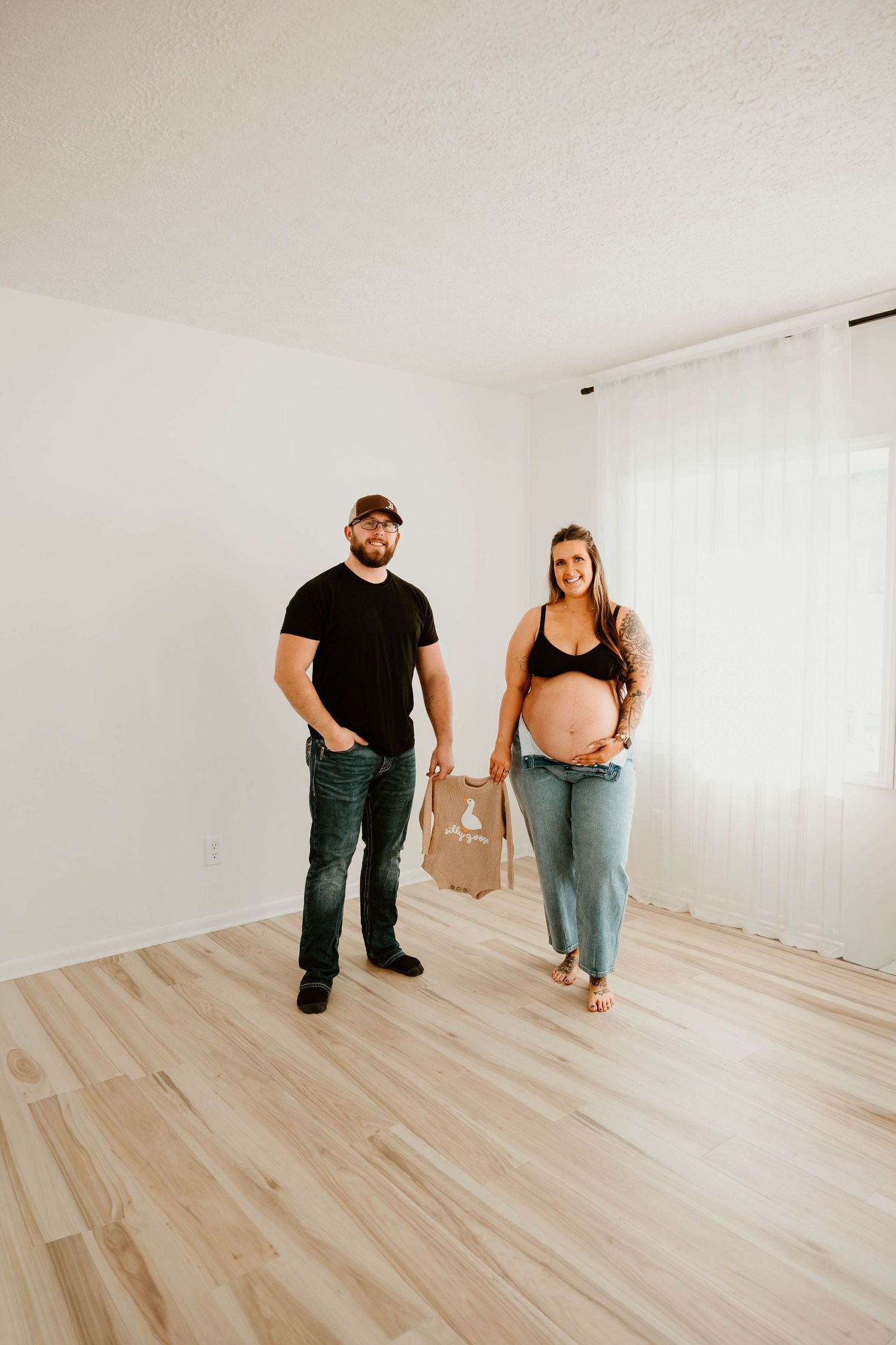 Couple standing together in empty room with light wooden floors.