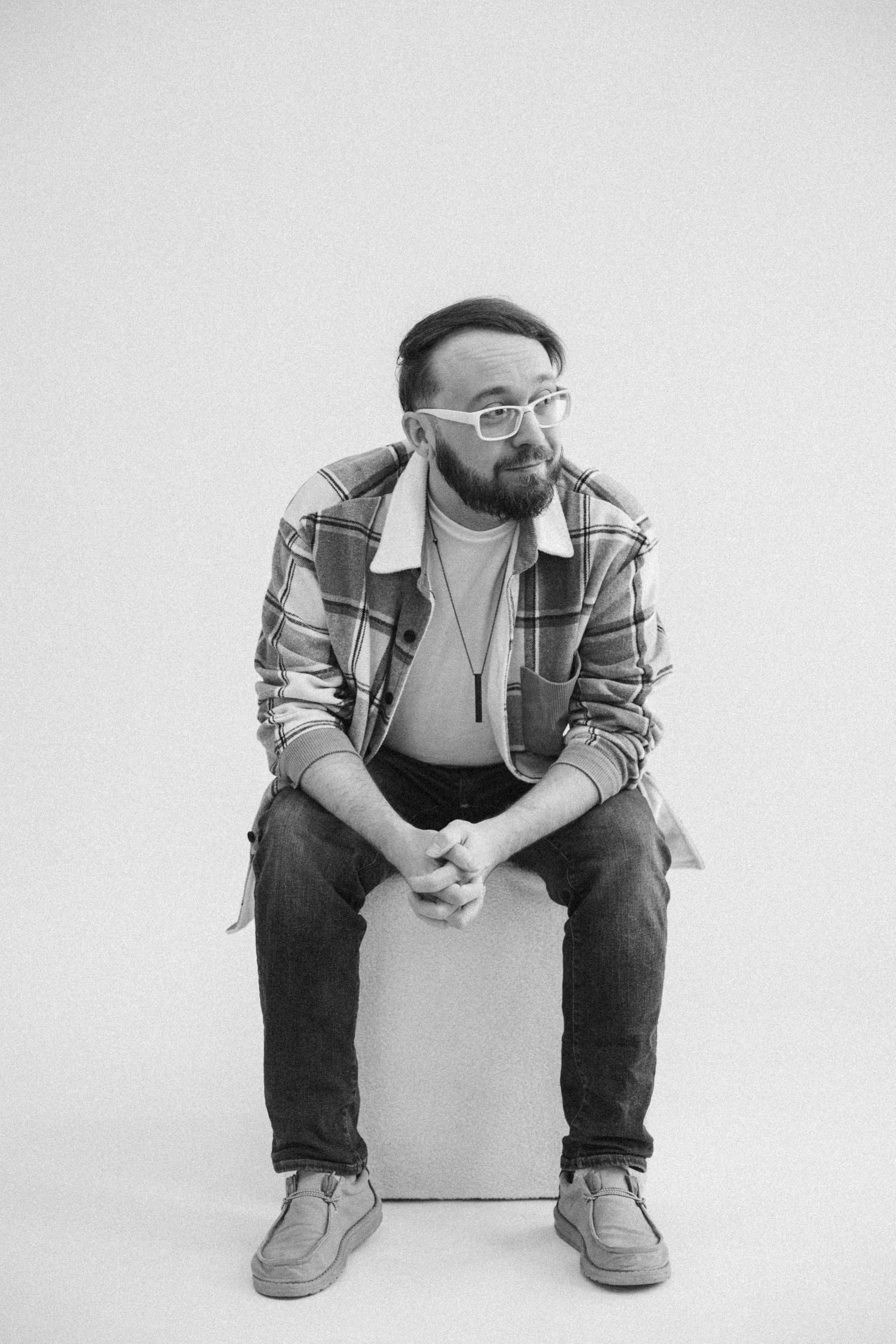 Person wearing glasses and plaid shirt seated in contemplative poses against white background.