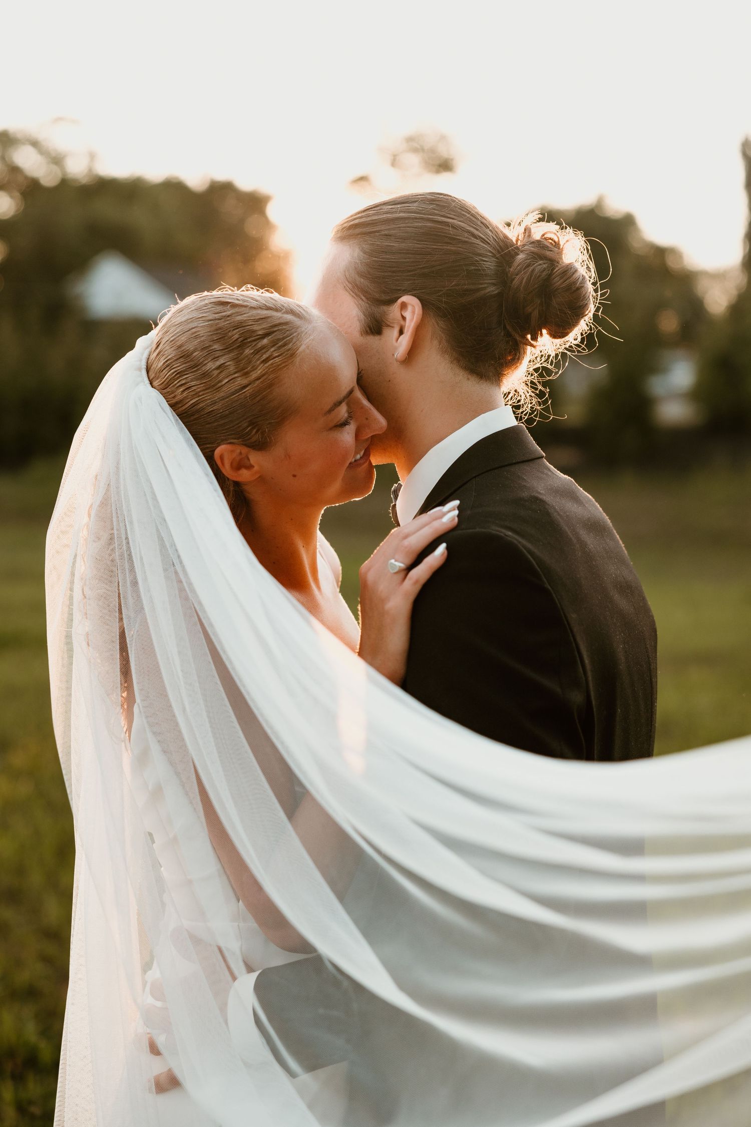 A flowing white veil catches the golden sunset light as newlyweds share a romantic moment.