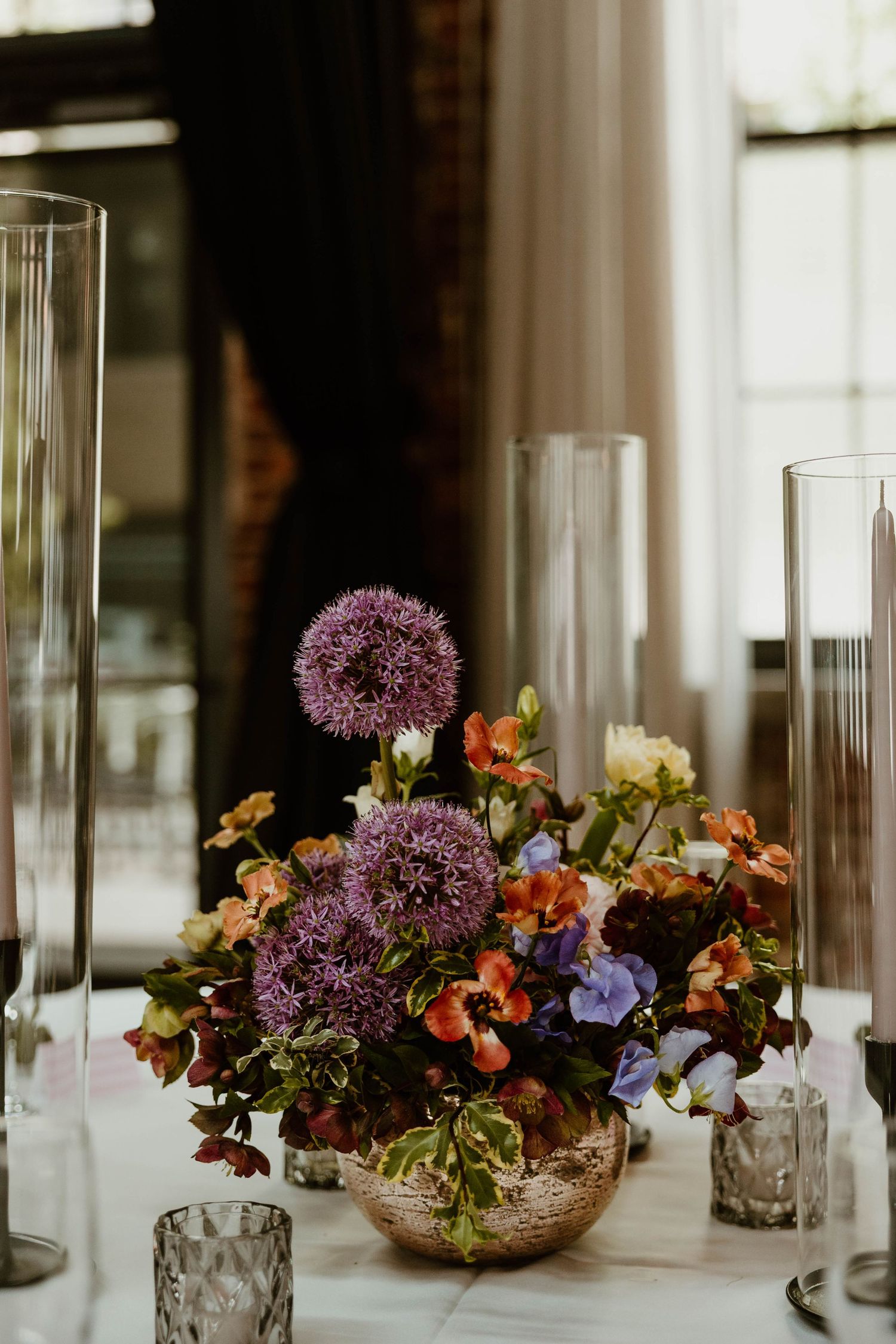 Elegant table centerpiece with purple and orange flowers in glass vases for wedding reception.