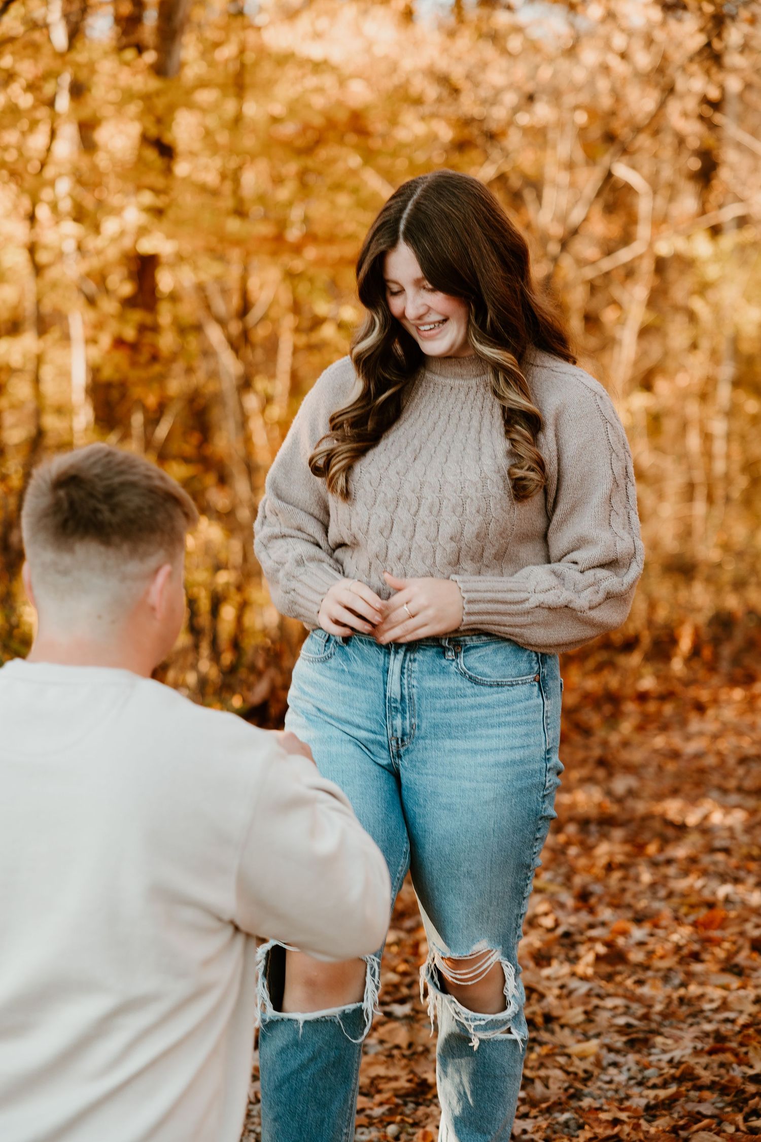 A romantic proposal moment captured in autumn woods with fallen leaves creating a golden backdrop.