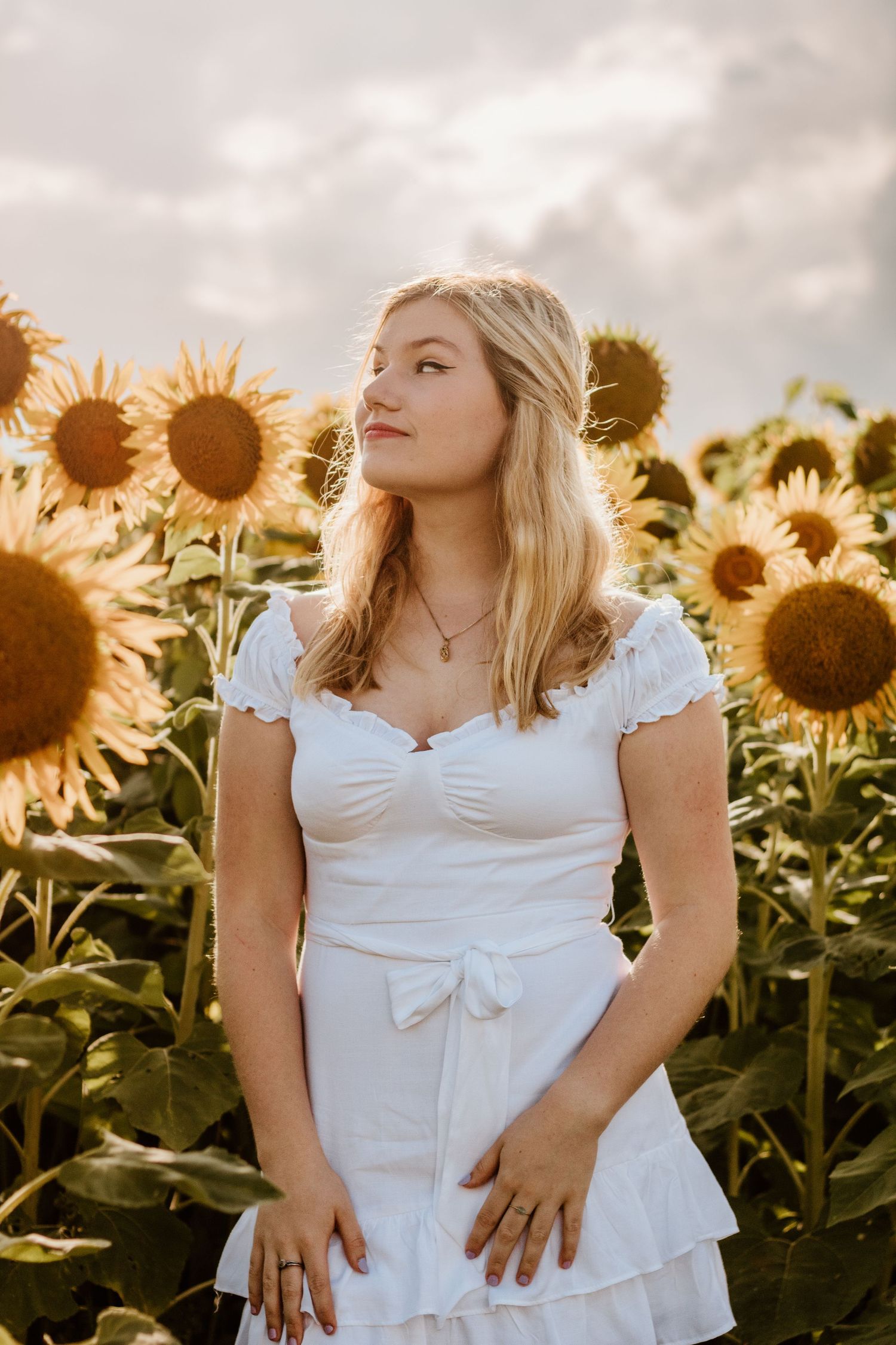 Candid poses in a sunflower field wearing a white peasant dress at golden hour.