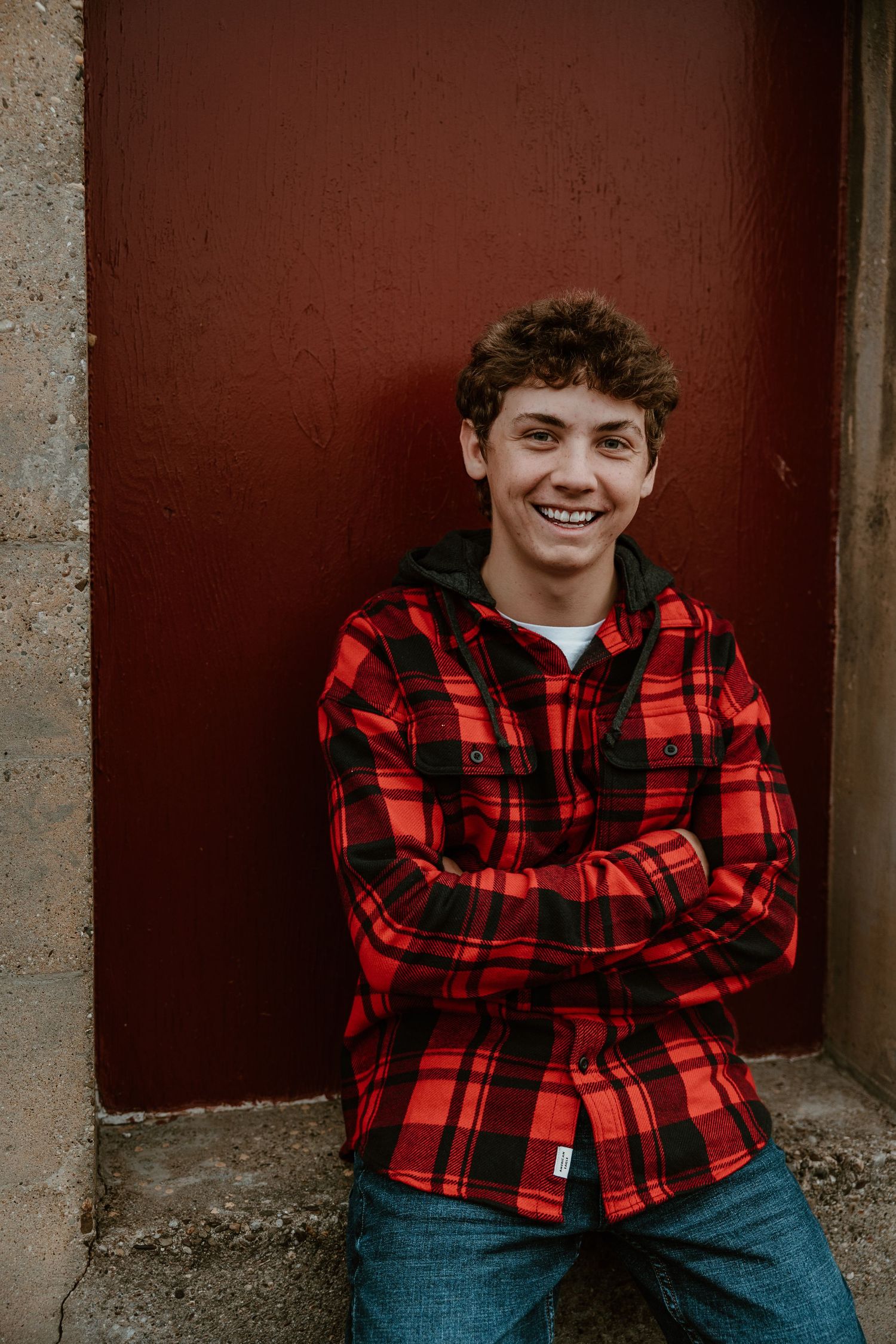 Person in red plaid flannel shirt sitting against dark red wall background.