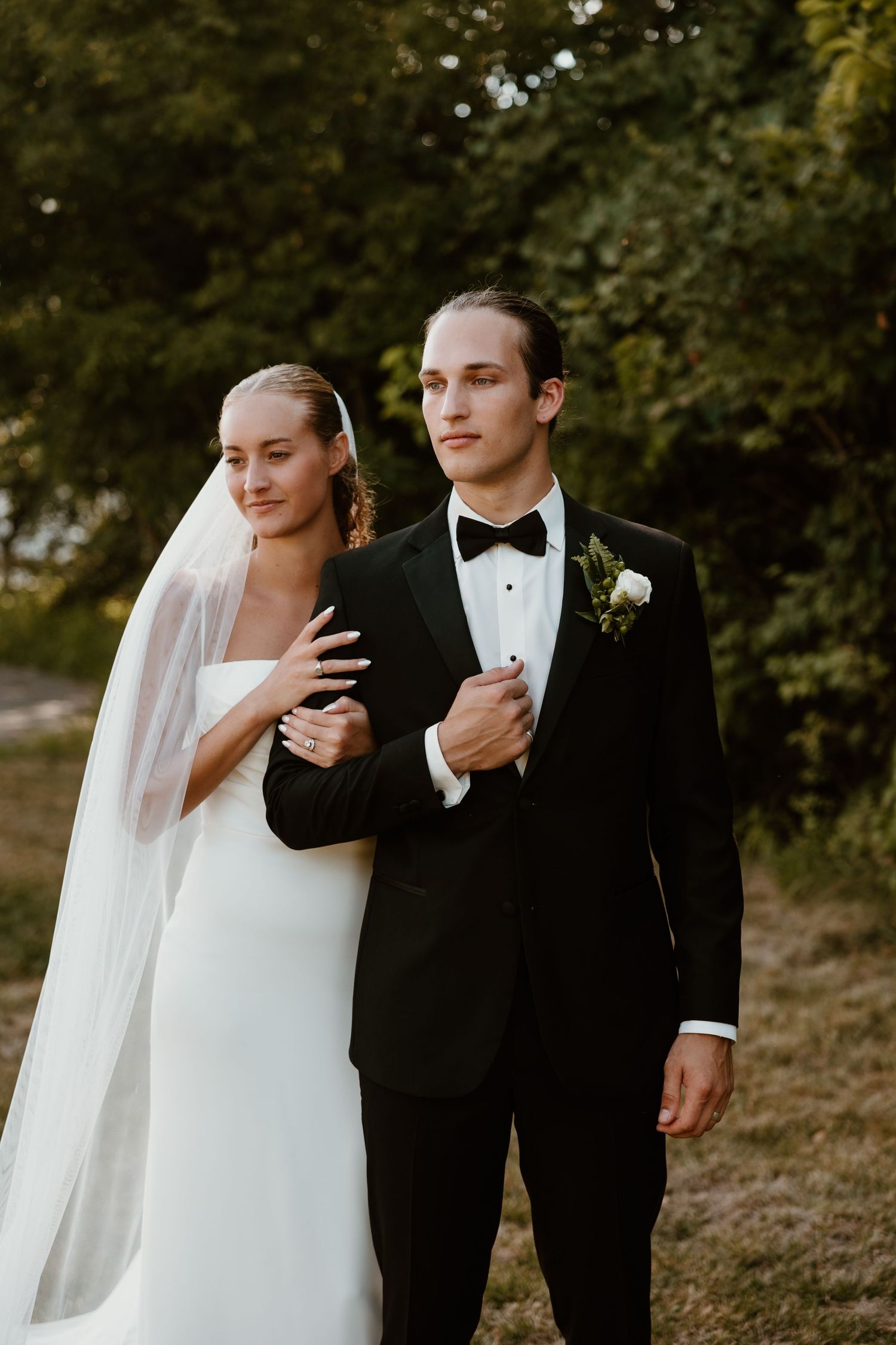 Elegant wedding couple walking together outdoors in formal attire with flowing veil.