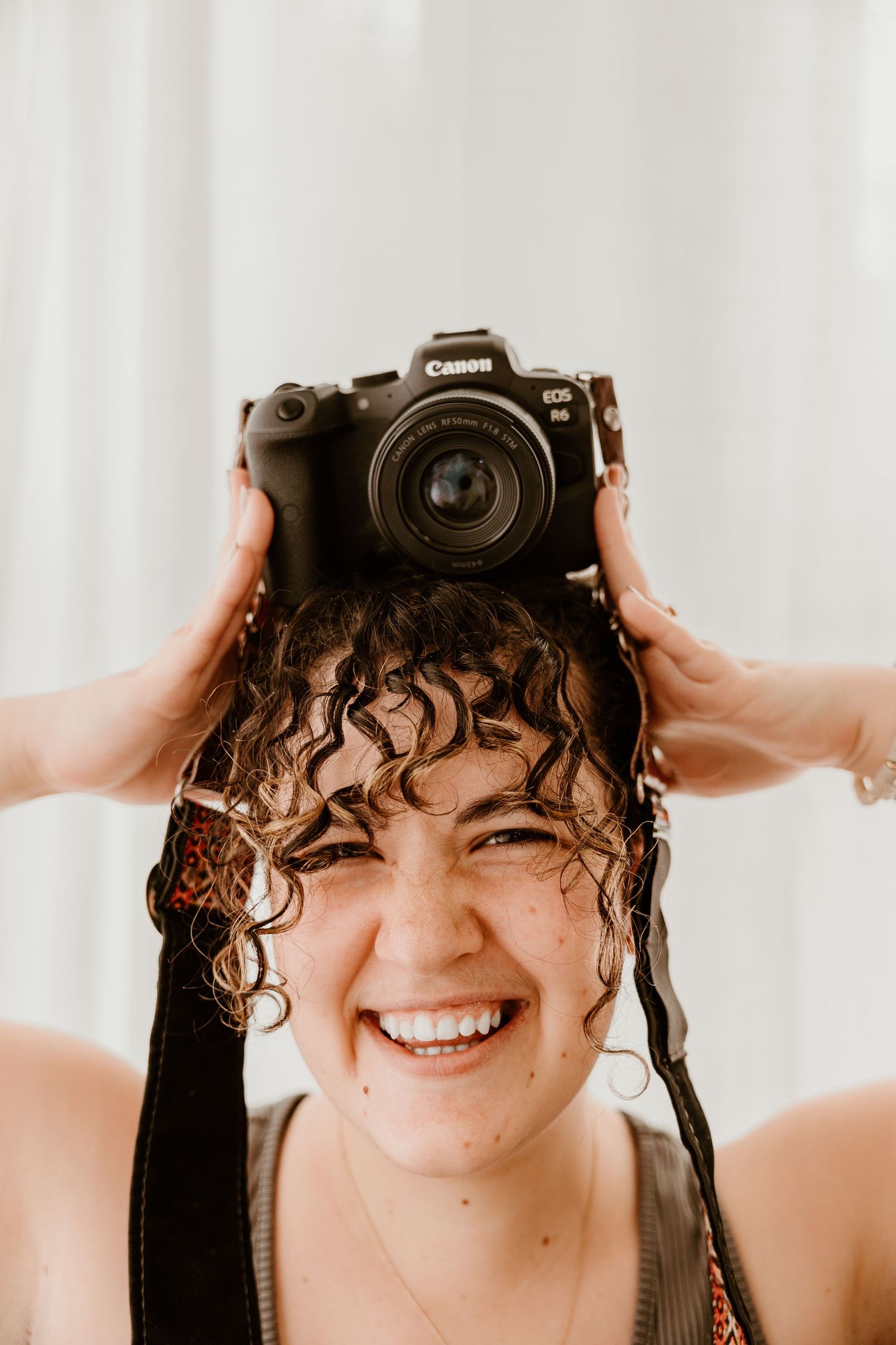 Person with curly hair playfully holds up a Canon camera in front of their face.