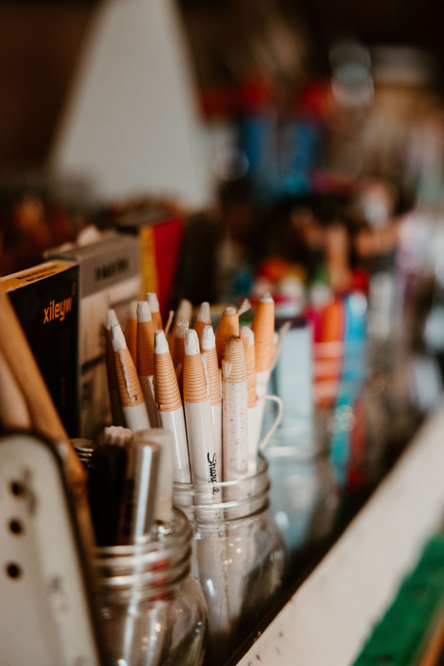 Collection of art markers and pens stored upright in clear glass jars.
