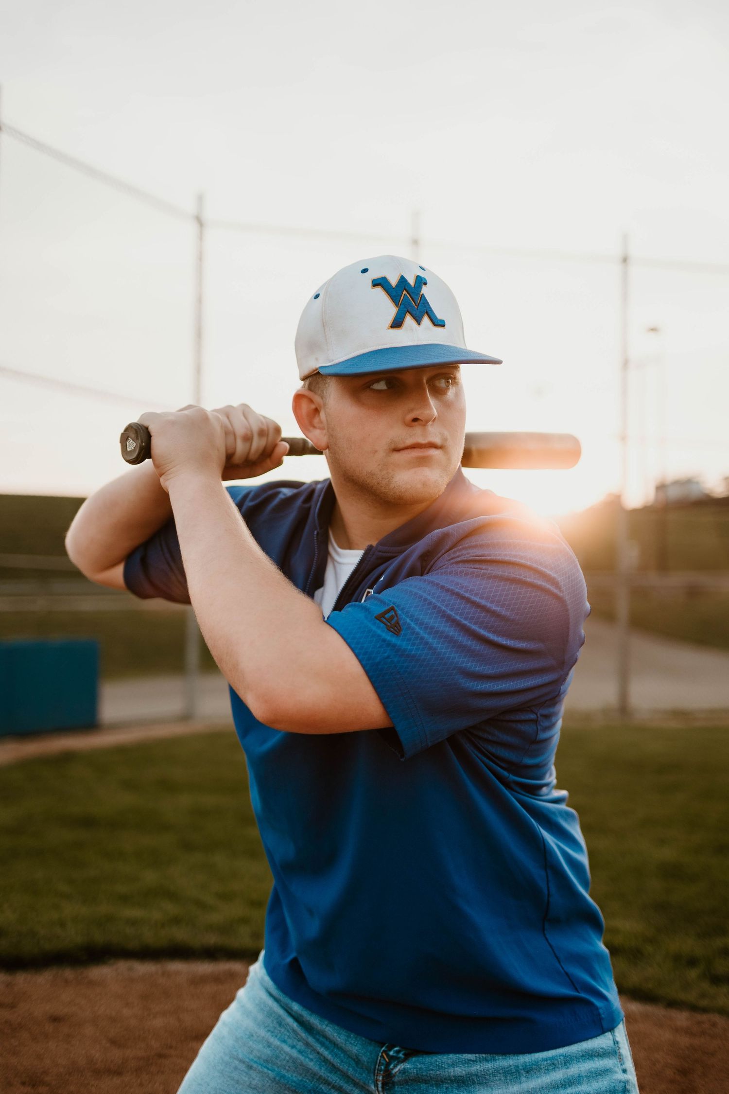 Baseball player in blue uniform practicing batting stance at sunset.