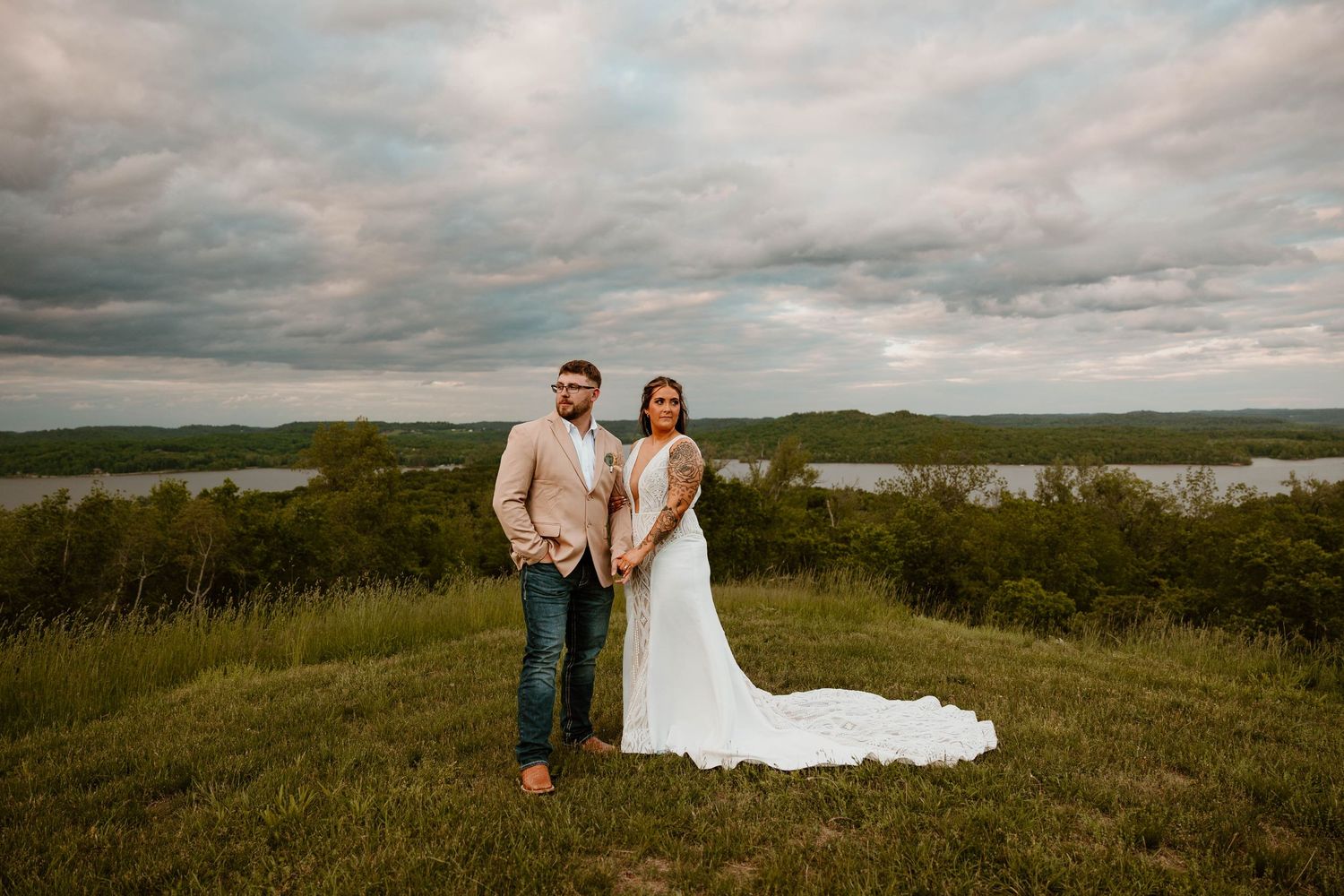 Panoramic landscape view of wedding couple in distance on hilltop during overcast day.