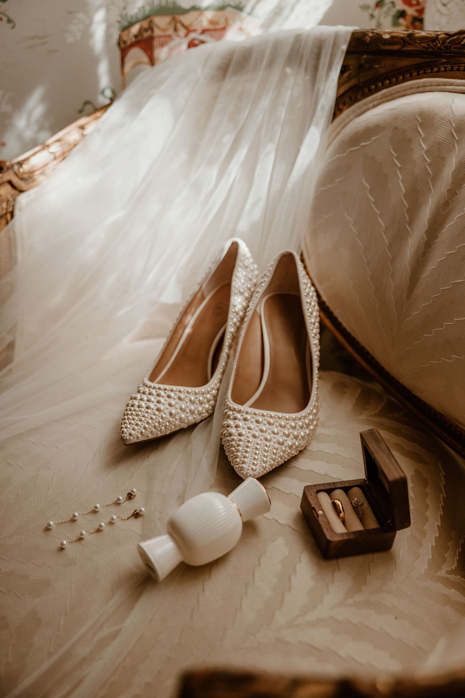 Pearl-embellished wedding heels and accessories arranged on white fabric.