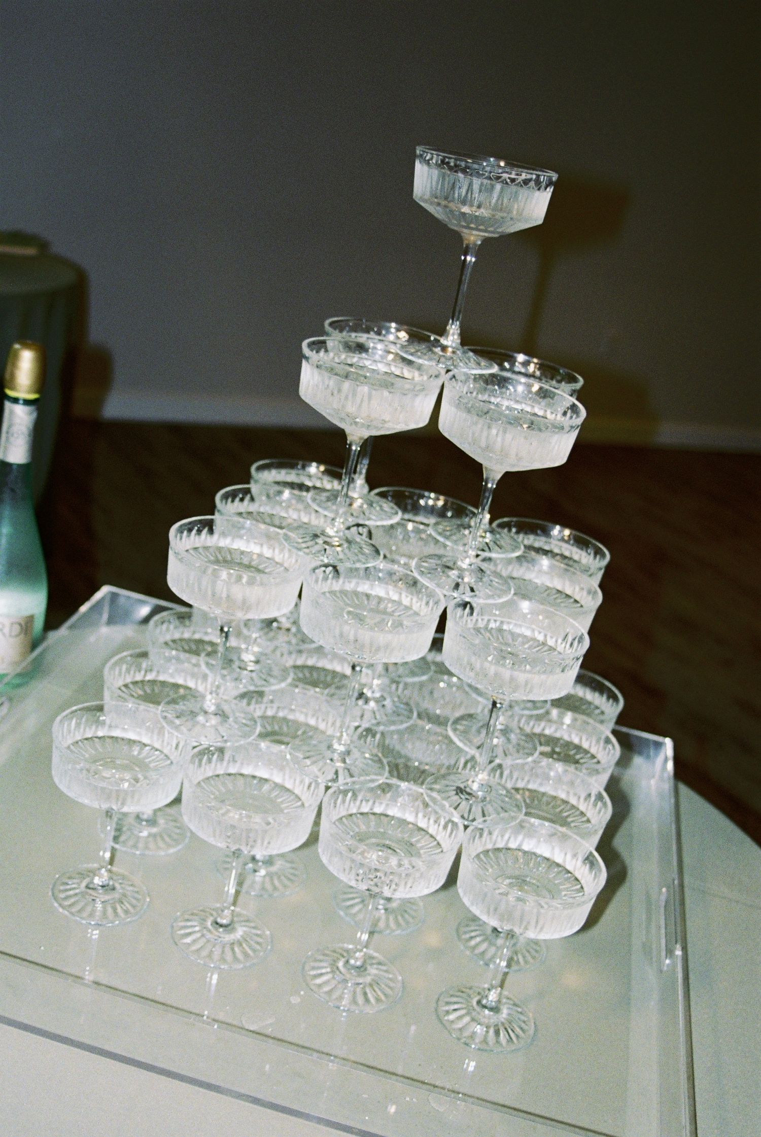 Elegant pyramid of crystal coupe champagne glasses arranged on mirrored tray for wedding reception.