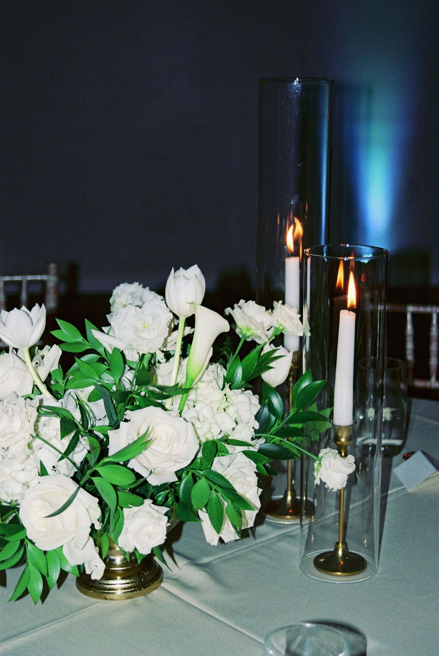 Elegant wedding centerpiece with white peonies, roses, and tall glass candle holders.