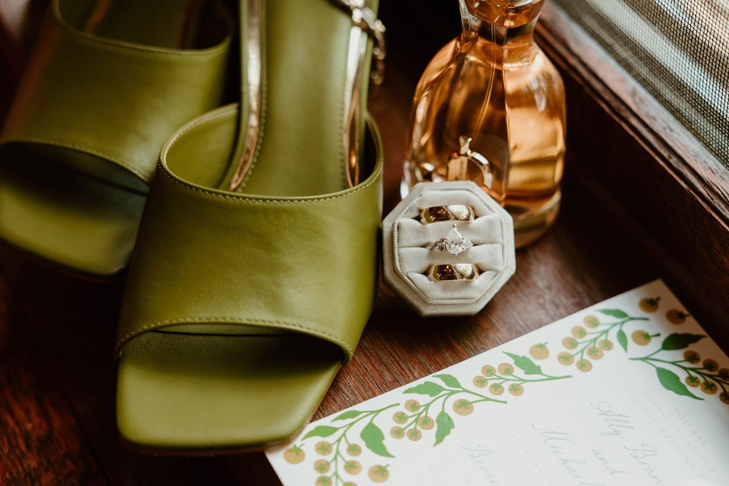 Green shoes and perfume bottle arranged with floral stationery on wooden surface.