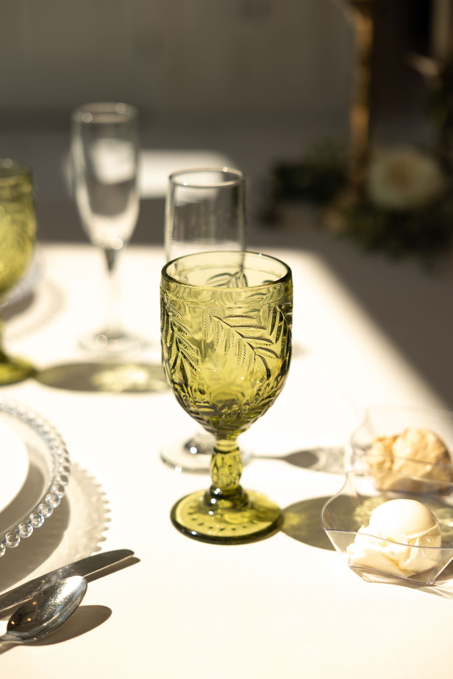 Vintage-style green glass goblets catch sunlight on an elegant wedding table setting.