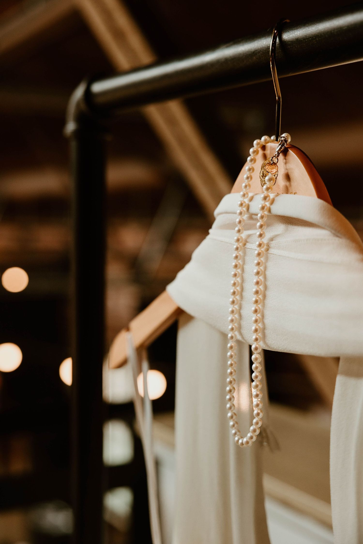 Pearl necklaces hanging elegantly on white dress hangers with soft lighting.