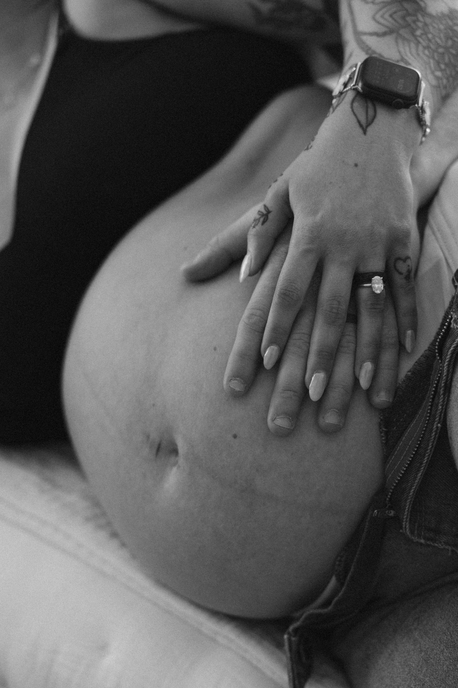 Close-up black and white photo of hands resting on pregnant belly.