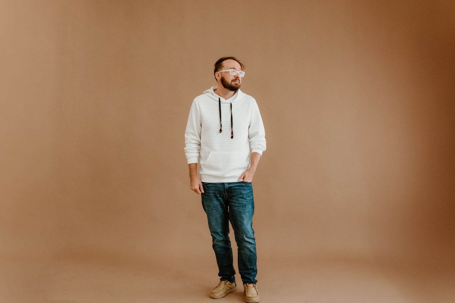 Person in hoodie and jeans posing against warm brown backdrop in casual portrait series.